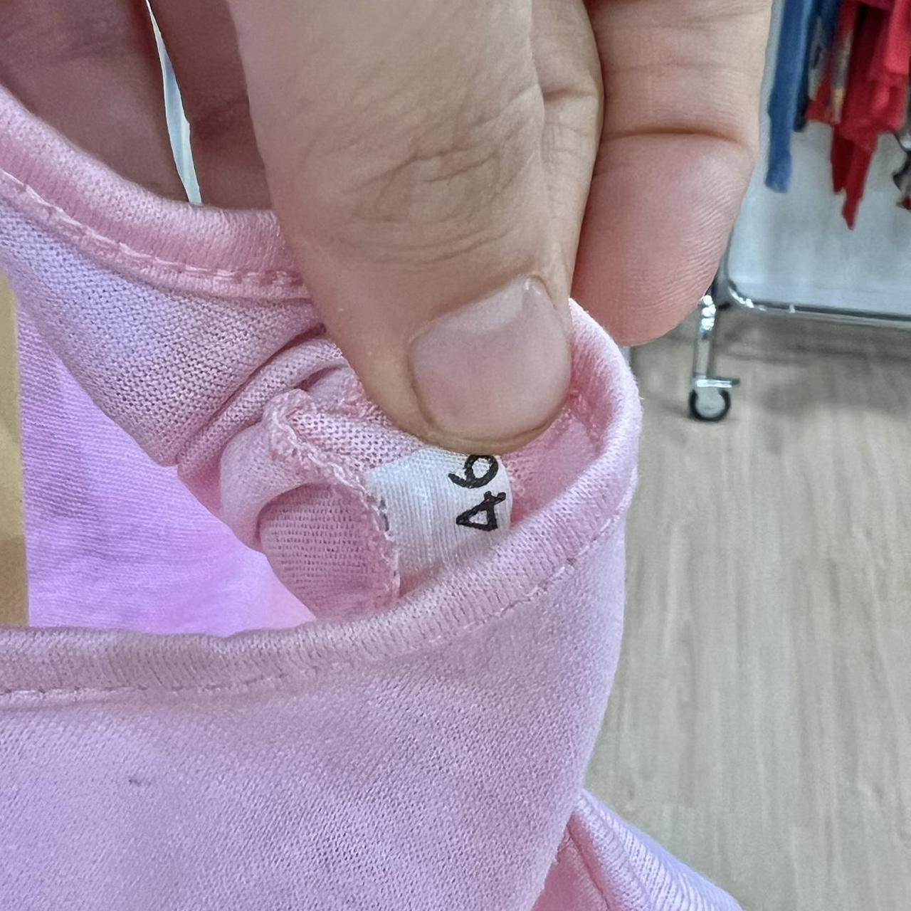 Close-up of a pink garment with a size tag held by a hand
