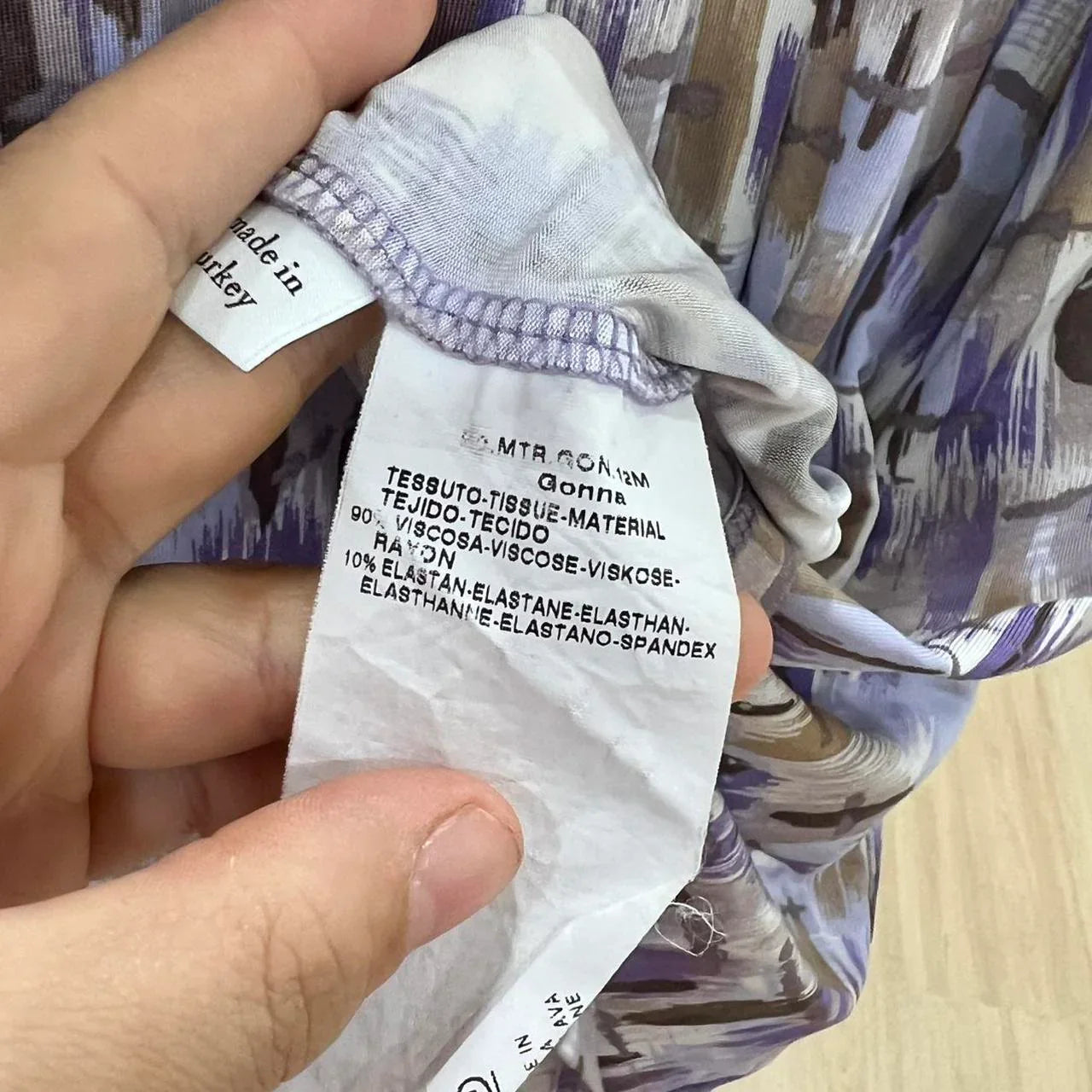 Hand holding clothing care label showing fabric composition viscose and spandex, abstract pattern