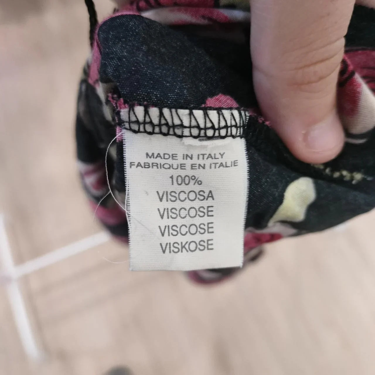 Clothing label reading 100% viscose, made in Italy, fabric tag on patterned fabric
