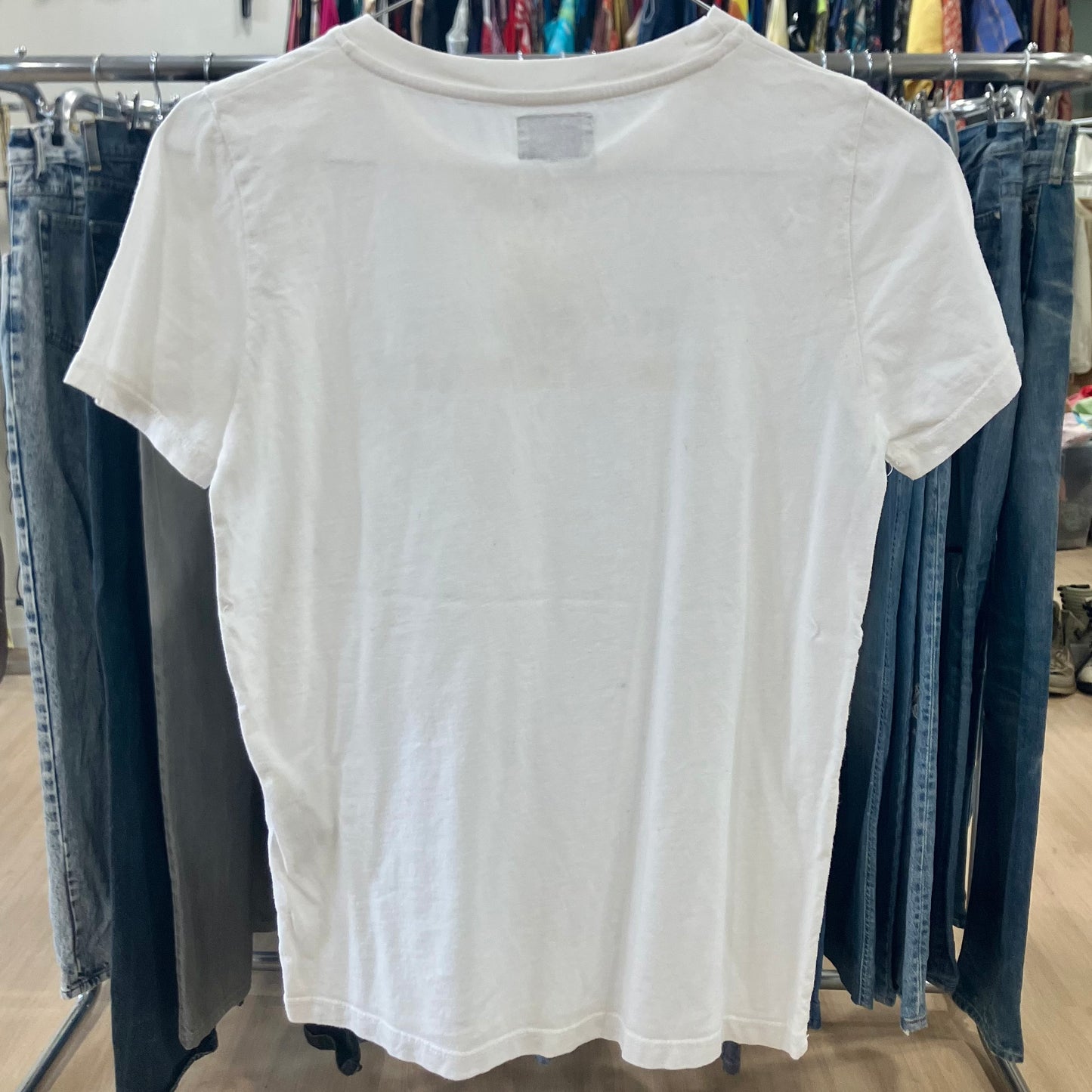 White t-shirt hanging on a rack with jeans in the background