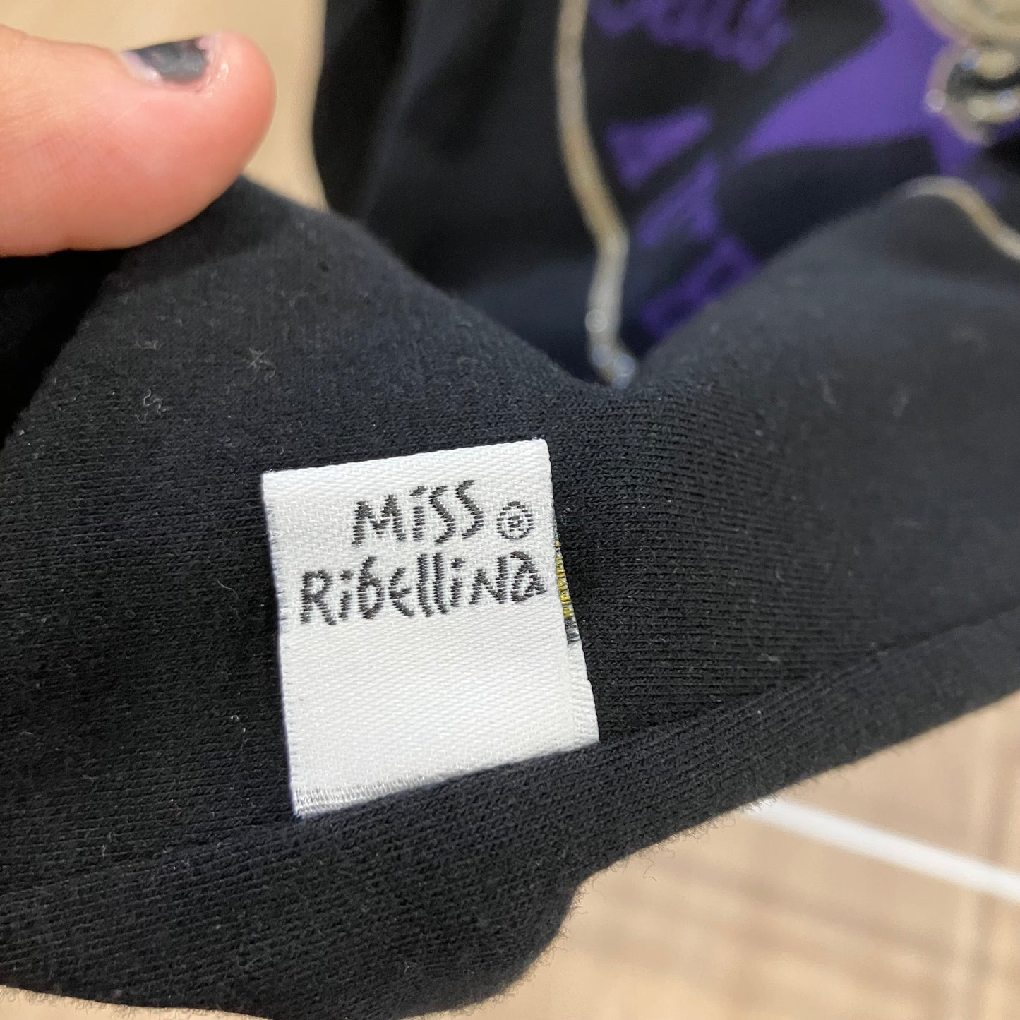 Black fabric with a 'Miss Ribellina' label held by a hand