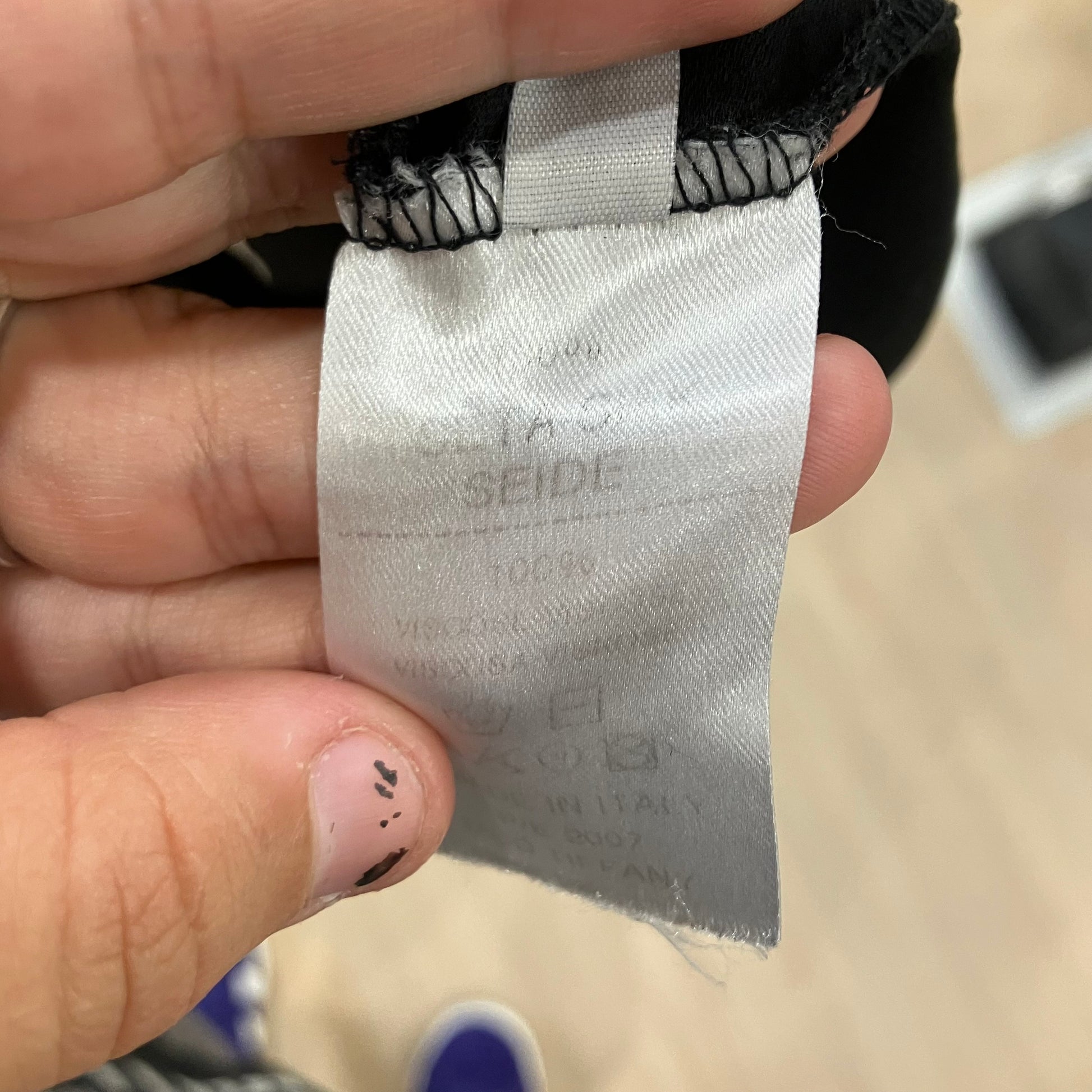 Close-up of a fabric tag held by a hand with a blurred background