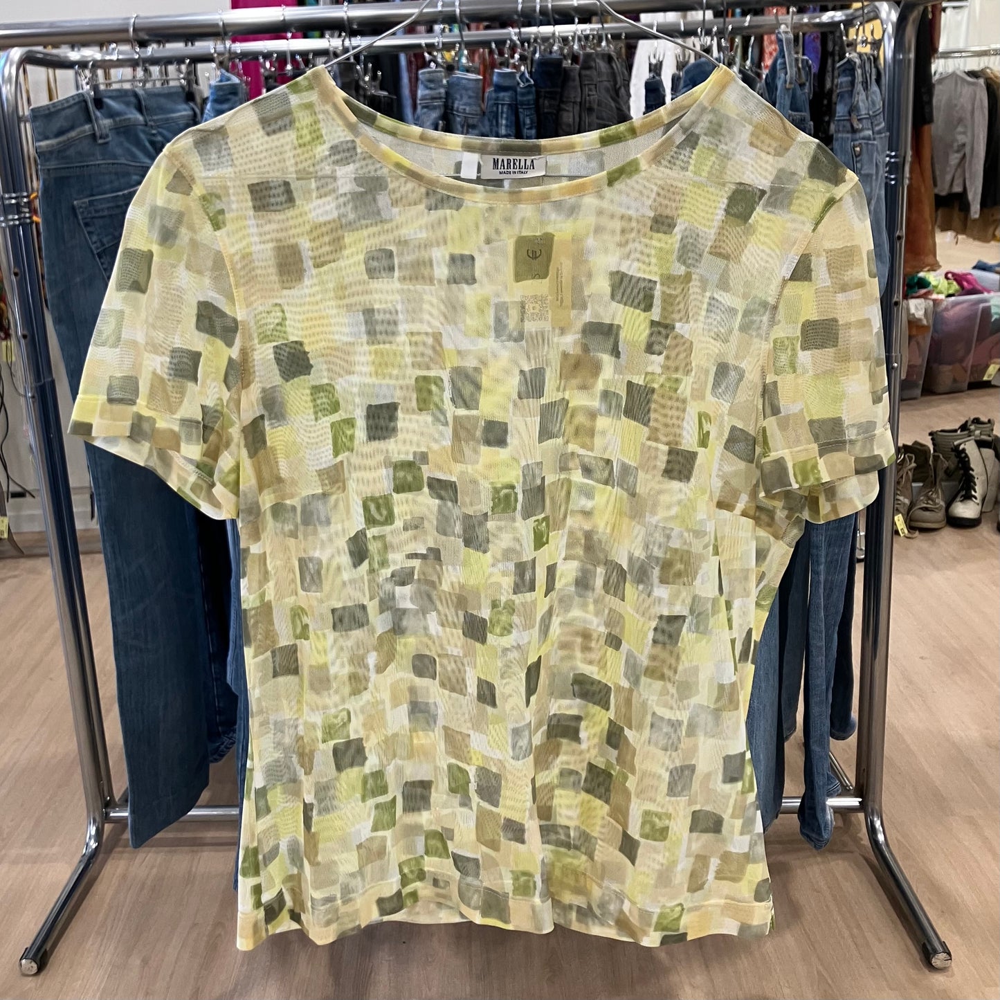 Green and yellow patterned shirt on a clothing rack with jeans in the background