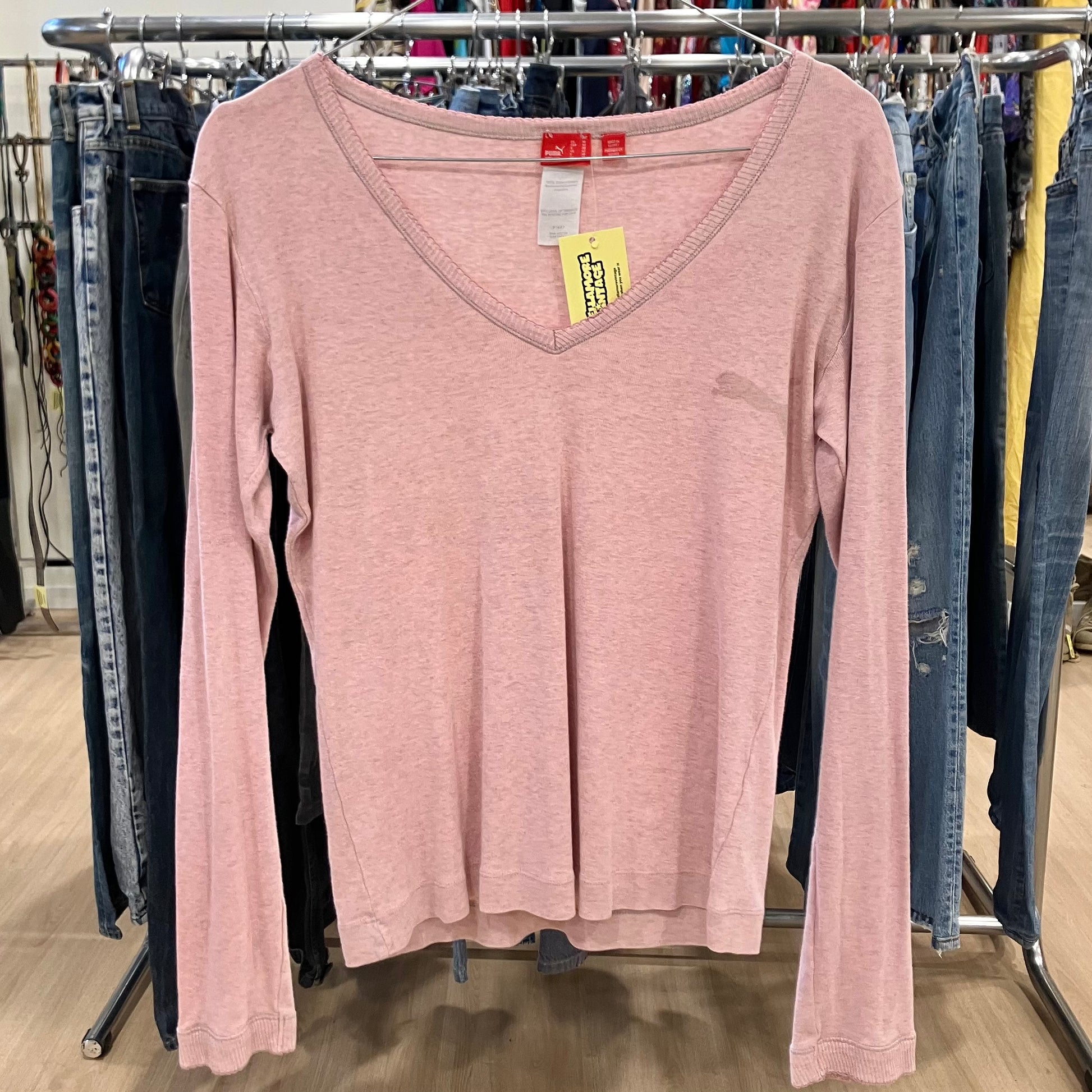Pink long-sleeve shirt with a tag on a clothing rack with jeans in the background