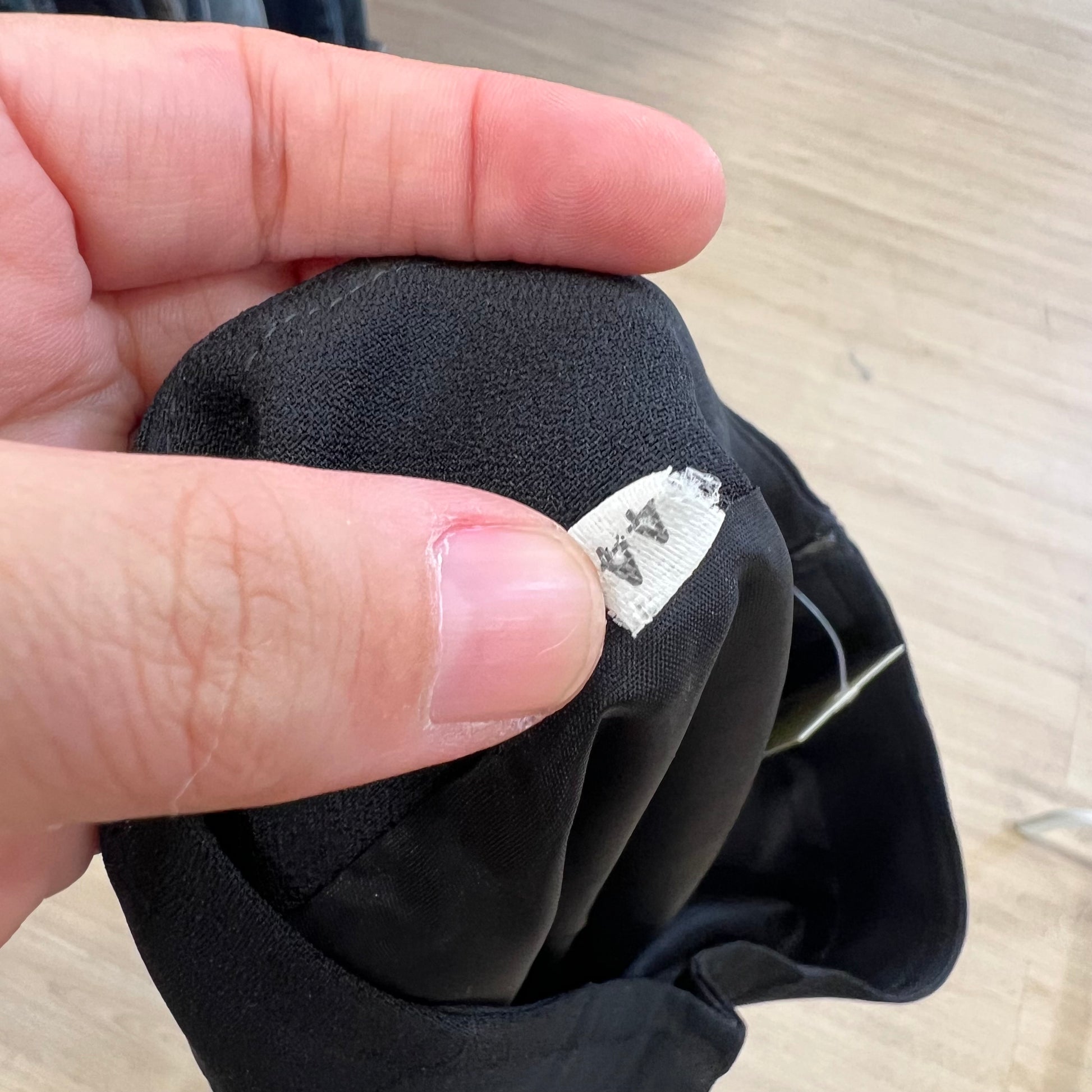 Hand holding a black fabric item with a visible label on a wooden surface