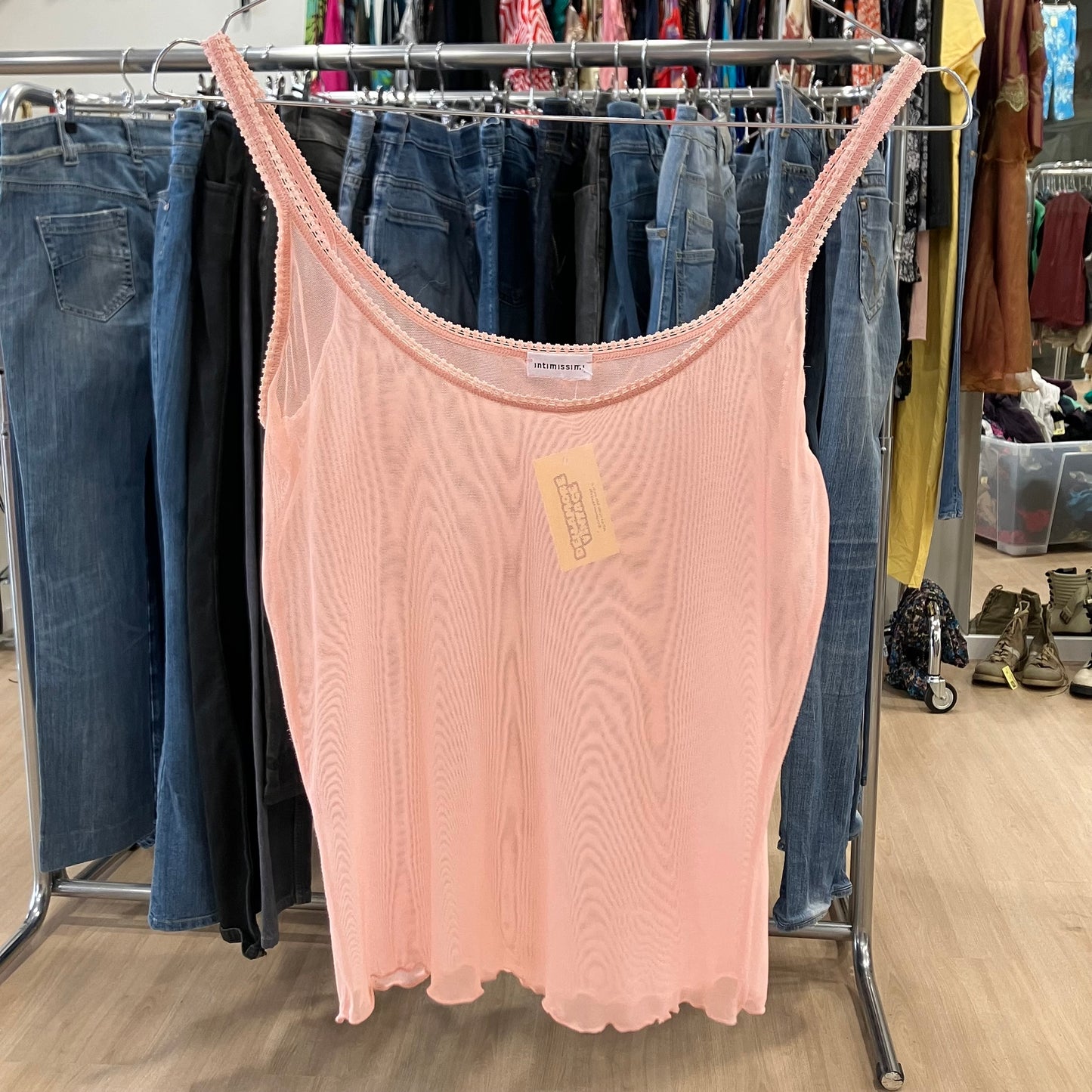Light pink sheer camisole tank top on hanger, displayed in second hand clothing store