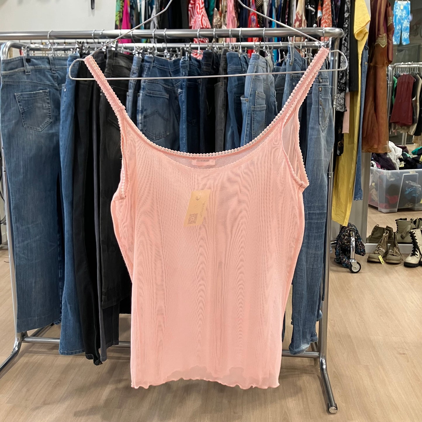 Light pink sleeveless tank top on hanger in second hand clothing store with jeans display