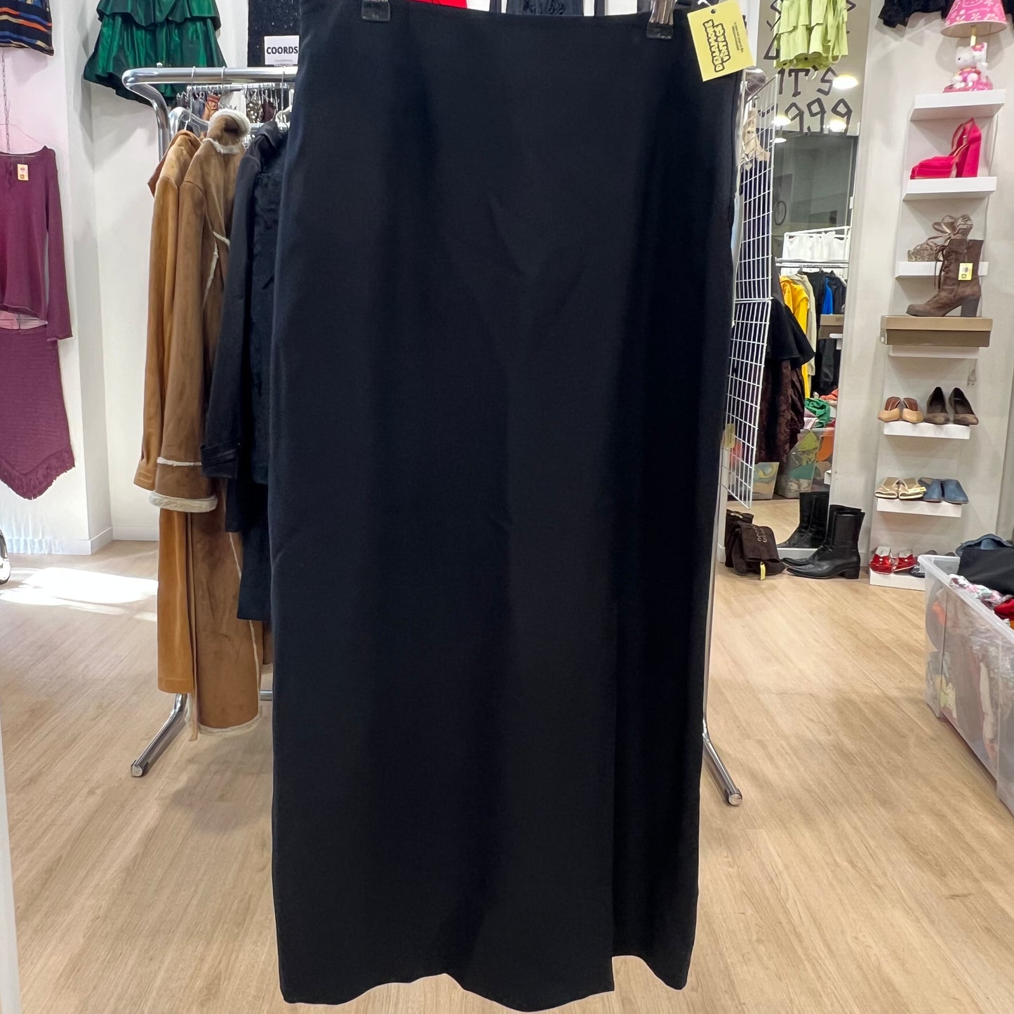 Black skirt hanging on a rack in a store with various clothing and shoes in the background