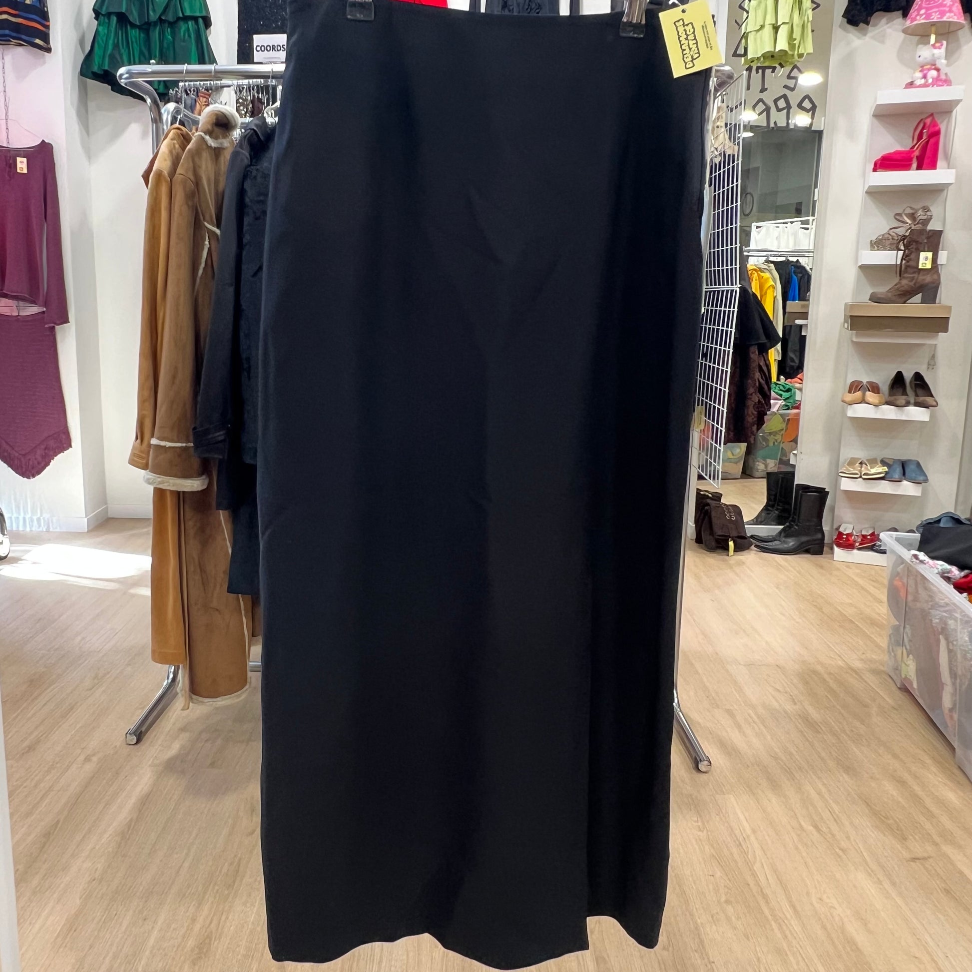 Black skirt hanging on a rack in a store with various clothing and shoes in the background