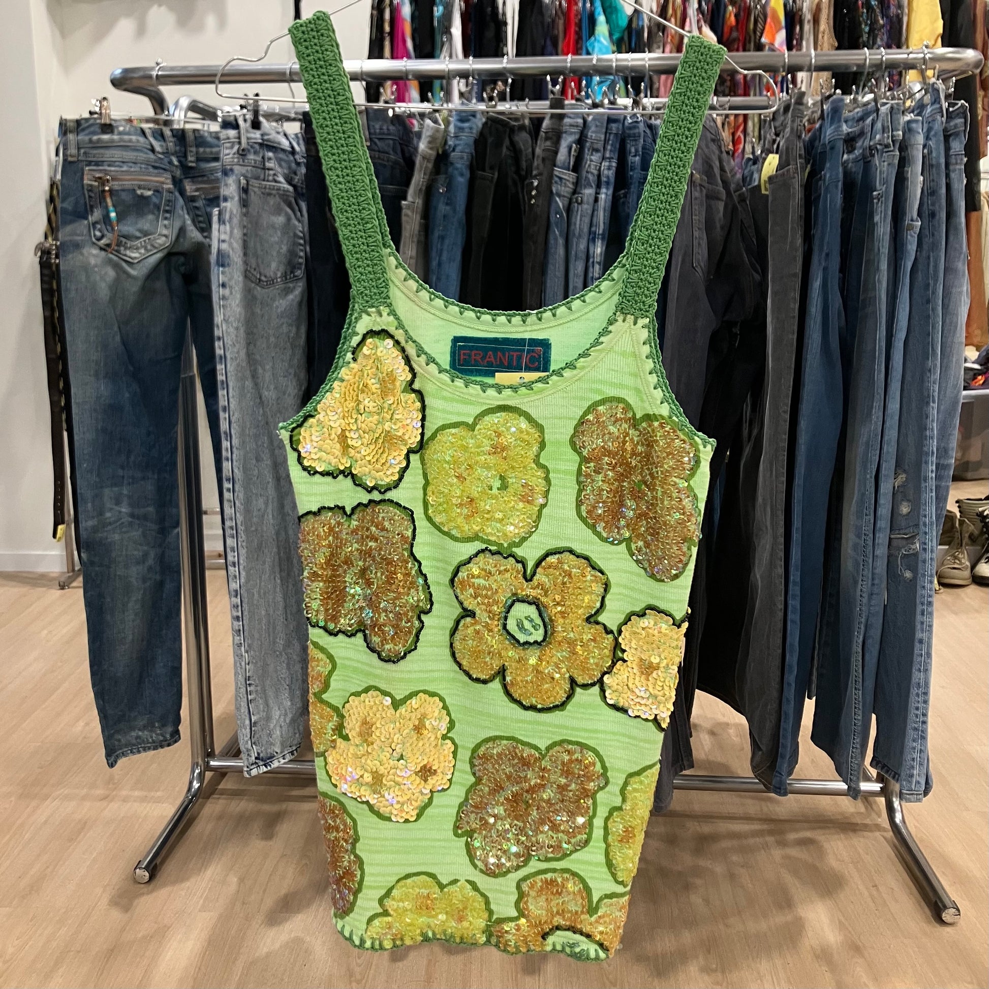Green sequined tank top with floral patterns hanging on a clothing rack