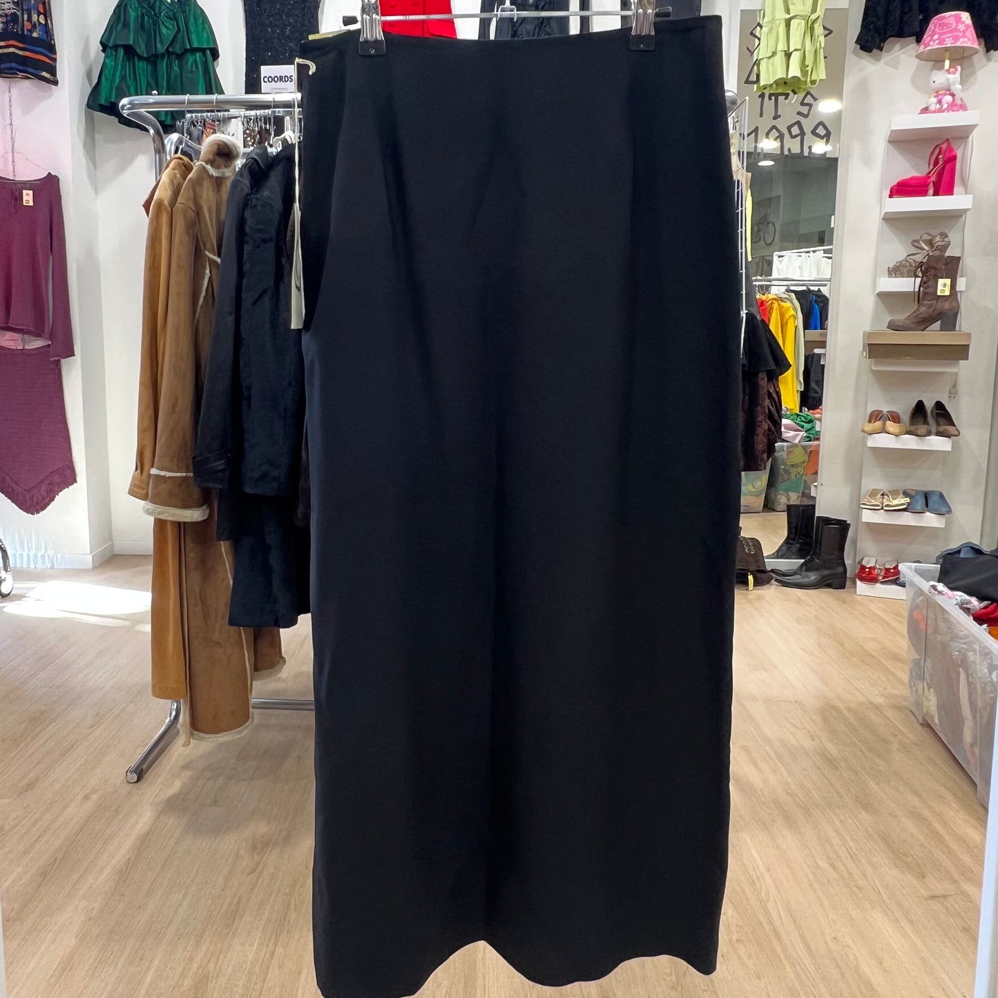 Black skirt hanging in a store with clothing racks and shelves in the background