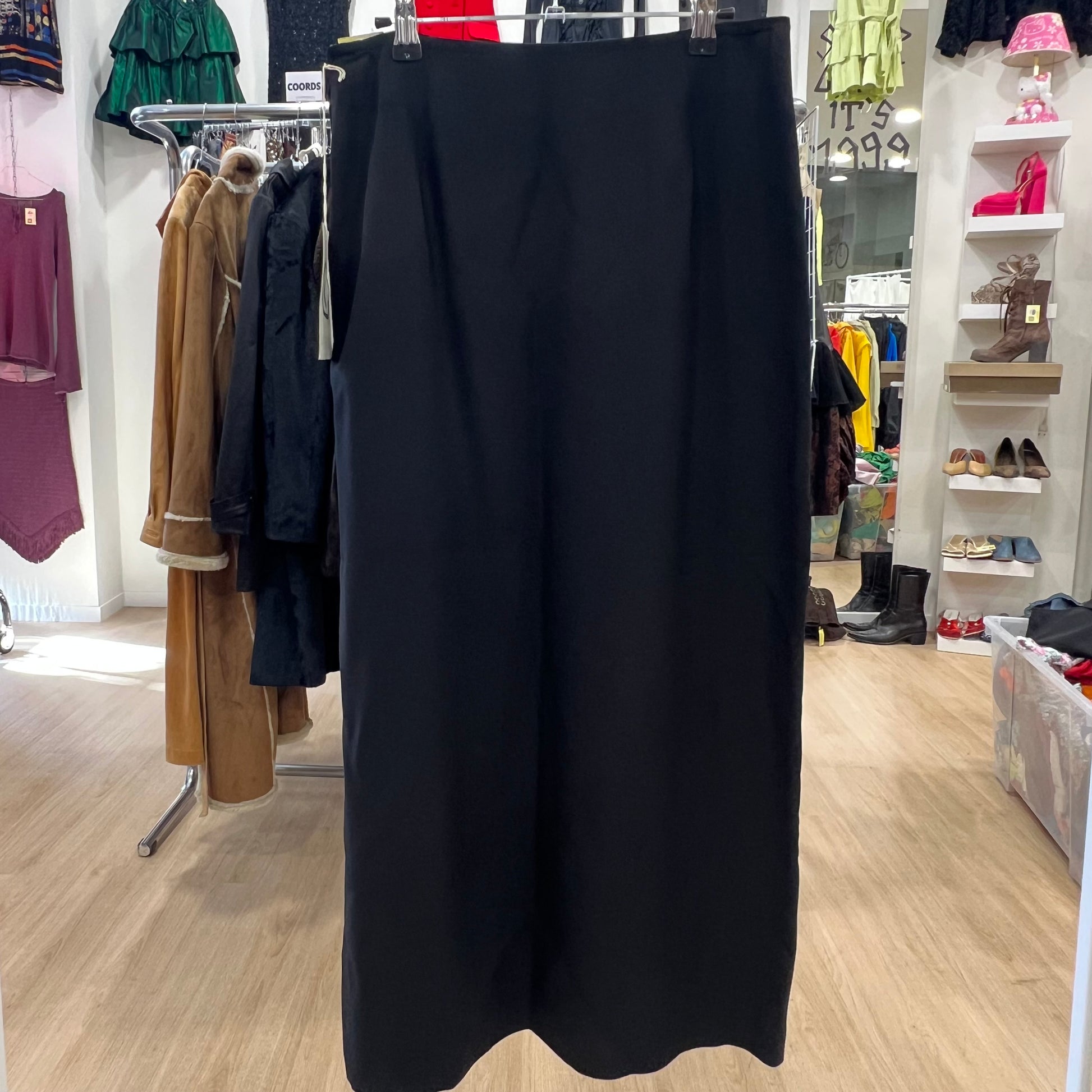 Black skirt hanging in a store with clothing racks and shelves in the background