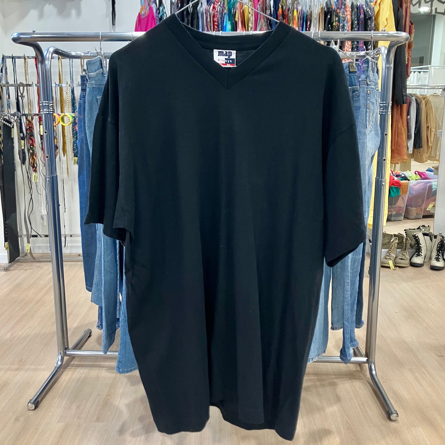 Black t-shirt on a hanger with a clothing rack and jeans in the background