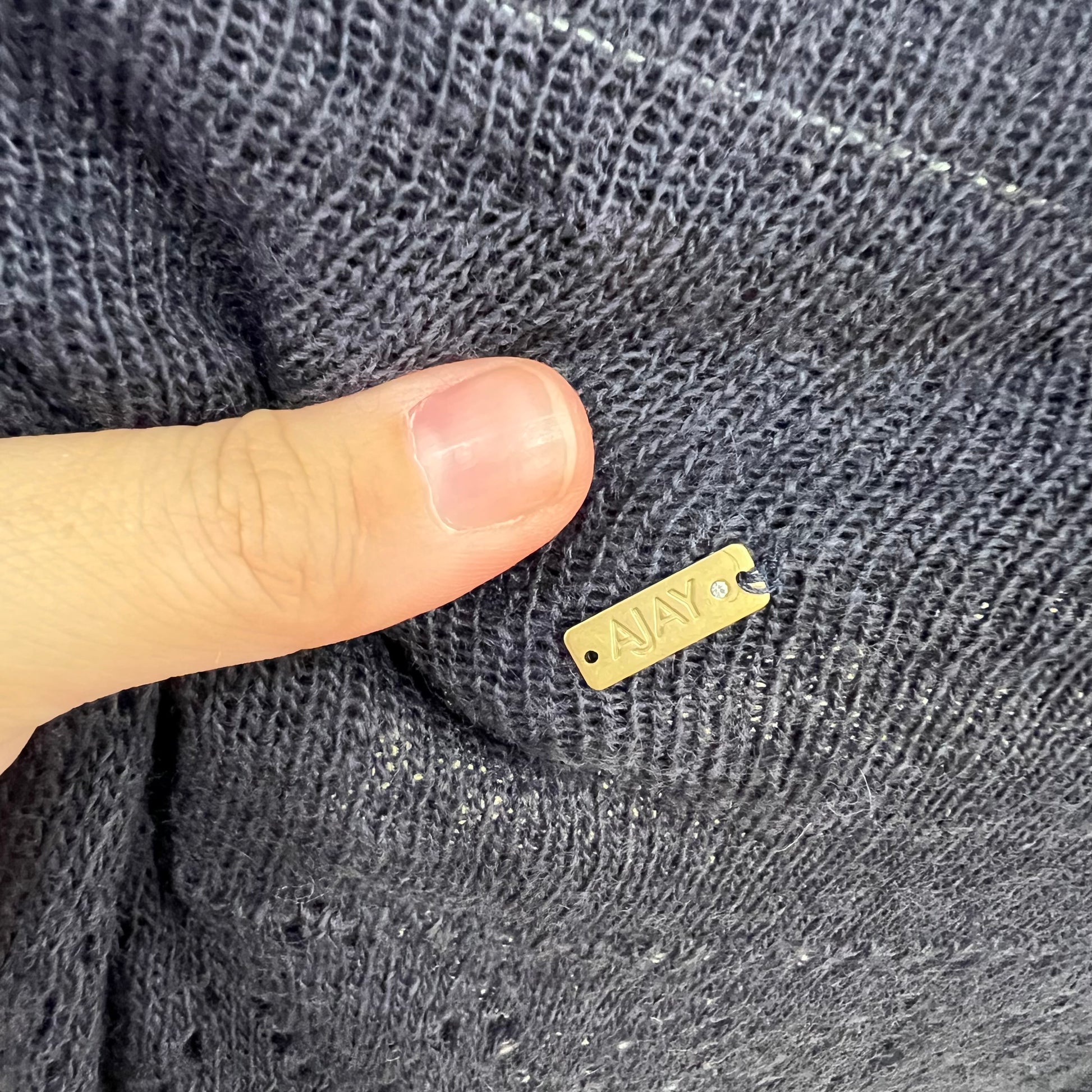 Gold tag on a textured gray fabric with a finger for scale