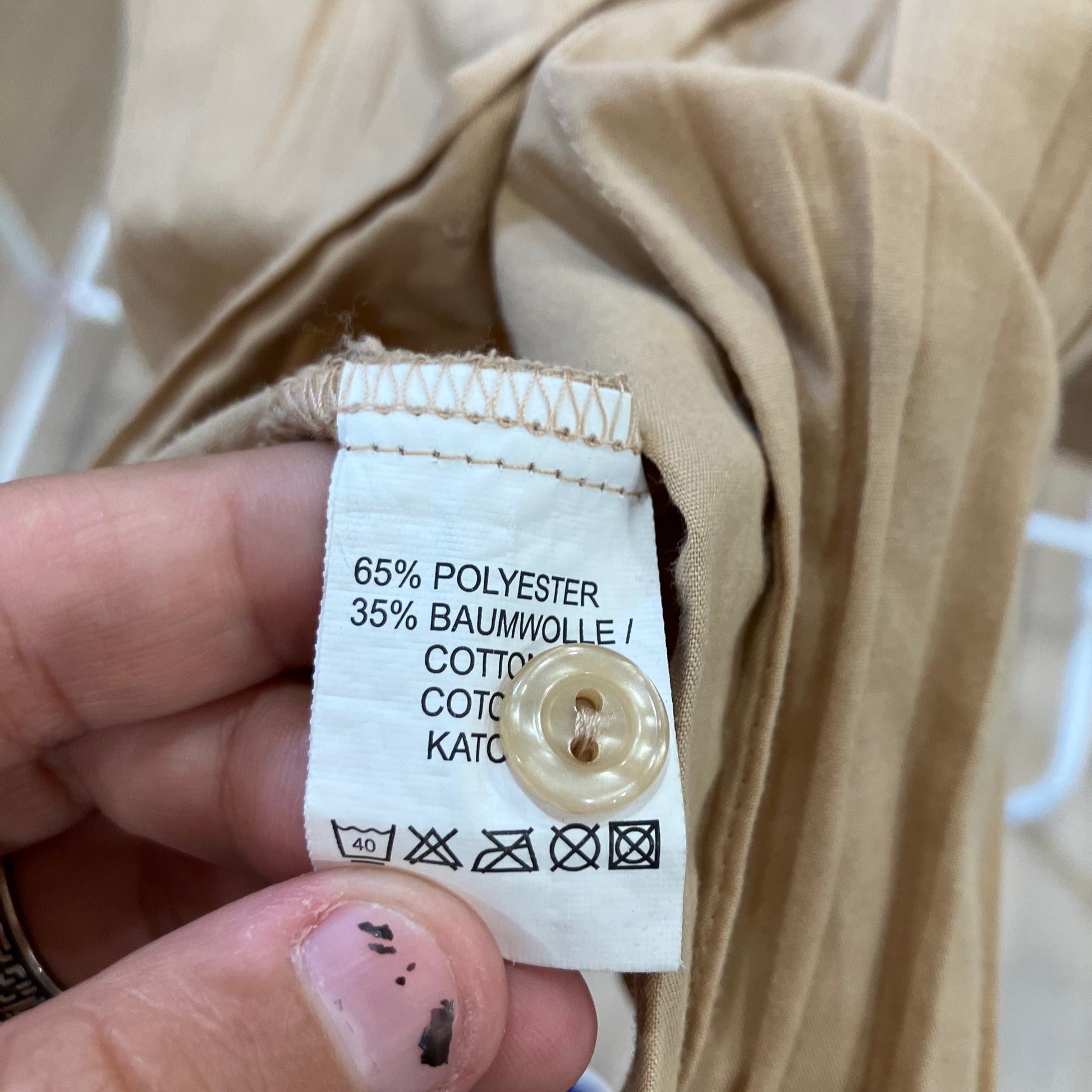 Clothing label with fabric composition details held by a hand against beige fabric
