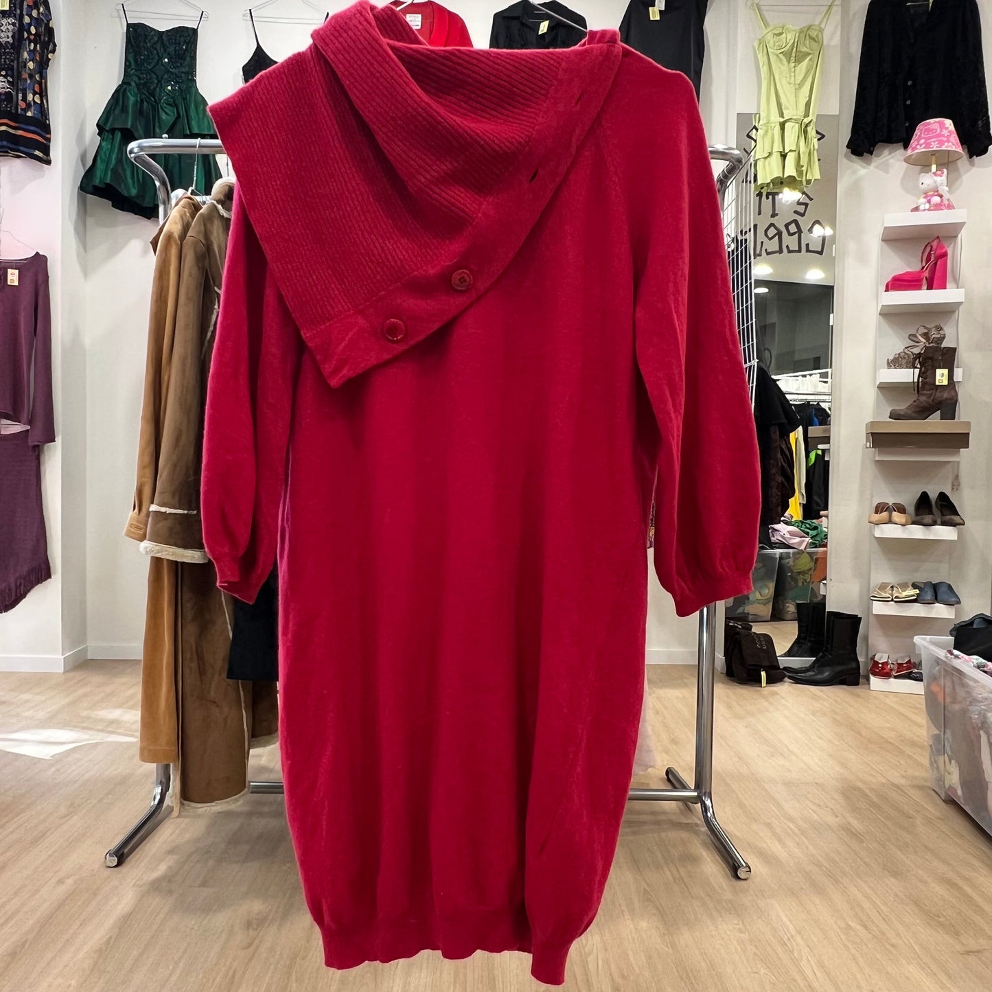 Red hoodie on a rack in a clothing store with various garments in the background.