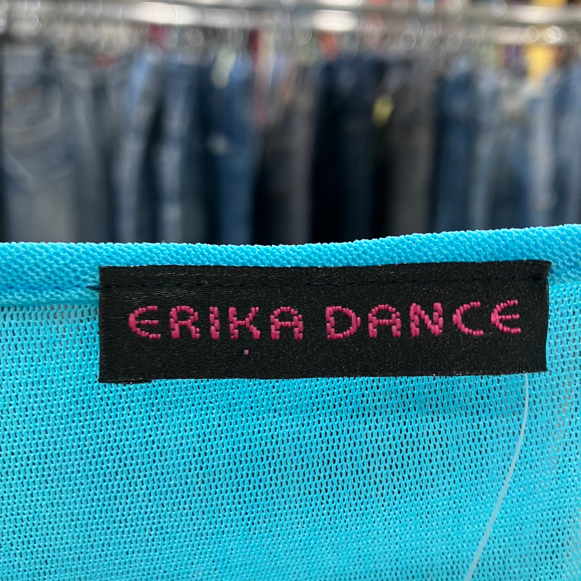 Close-up of a blue fabric with 'ERIKA DANCE' label against a blurred clothing background