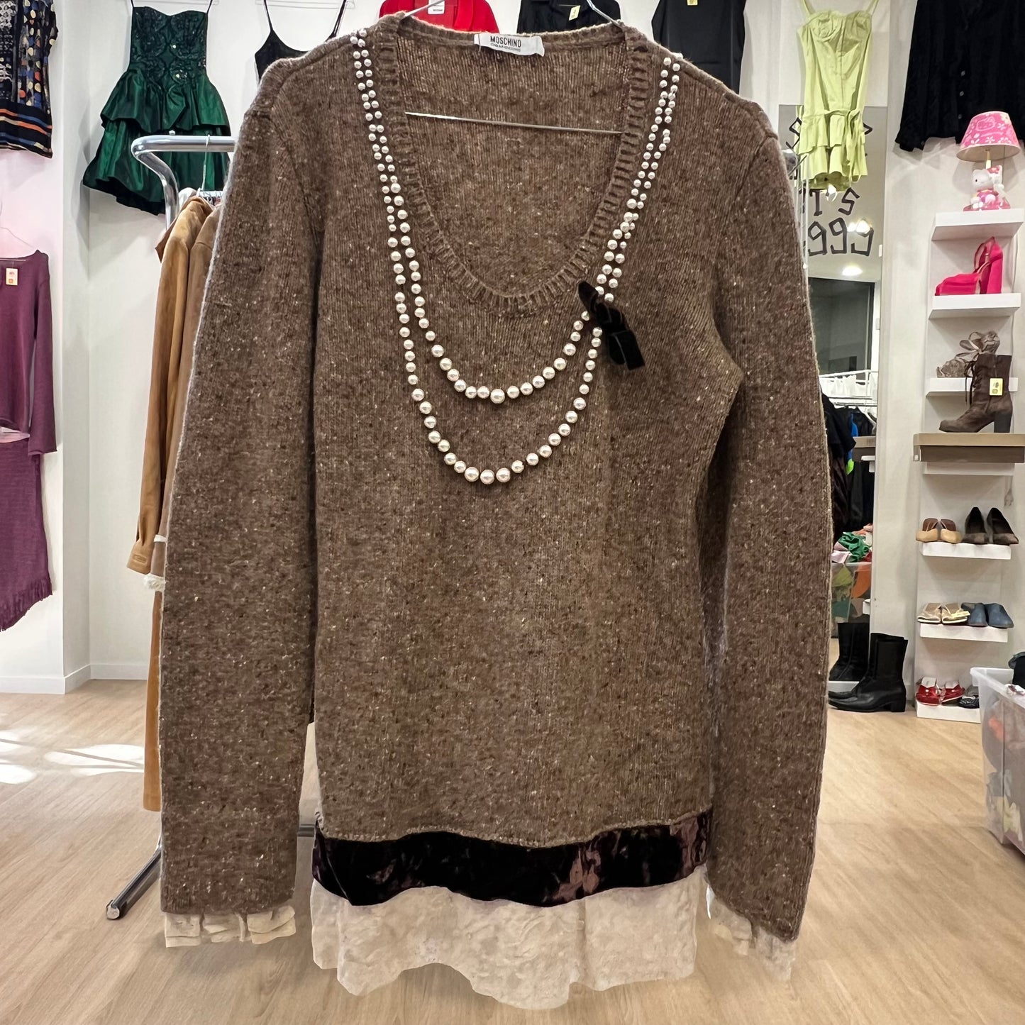 Brown sweater with pearl necklace on a rack in a store setting