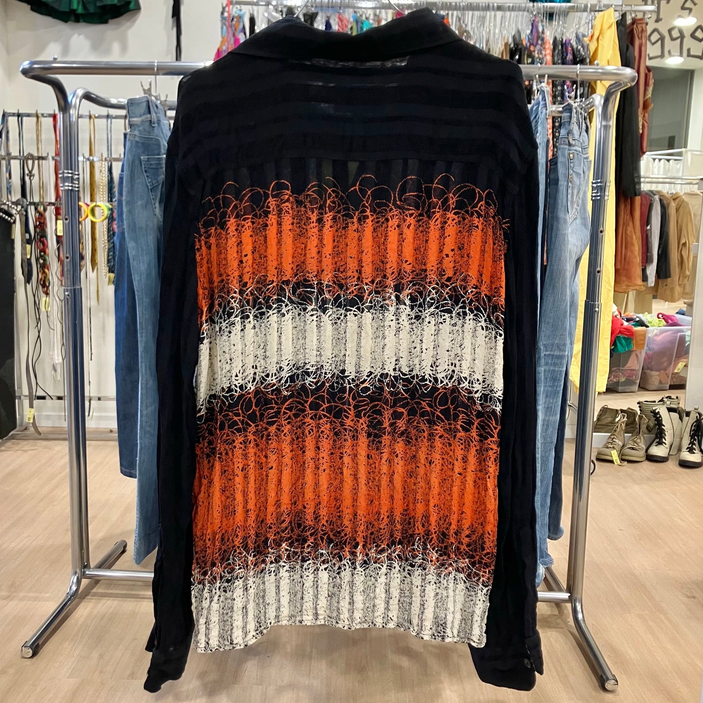 Black shirt with orange, white, and gray pattern on a clothing rack in a store