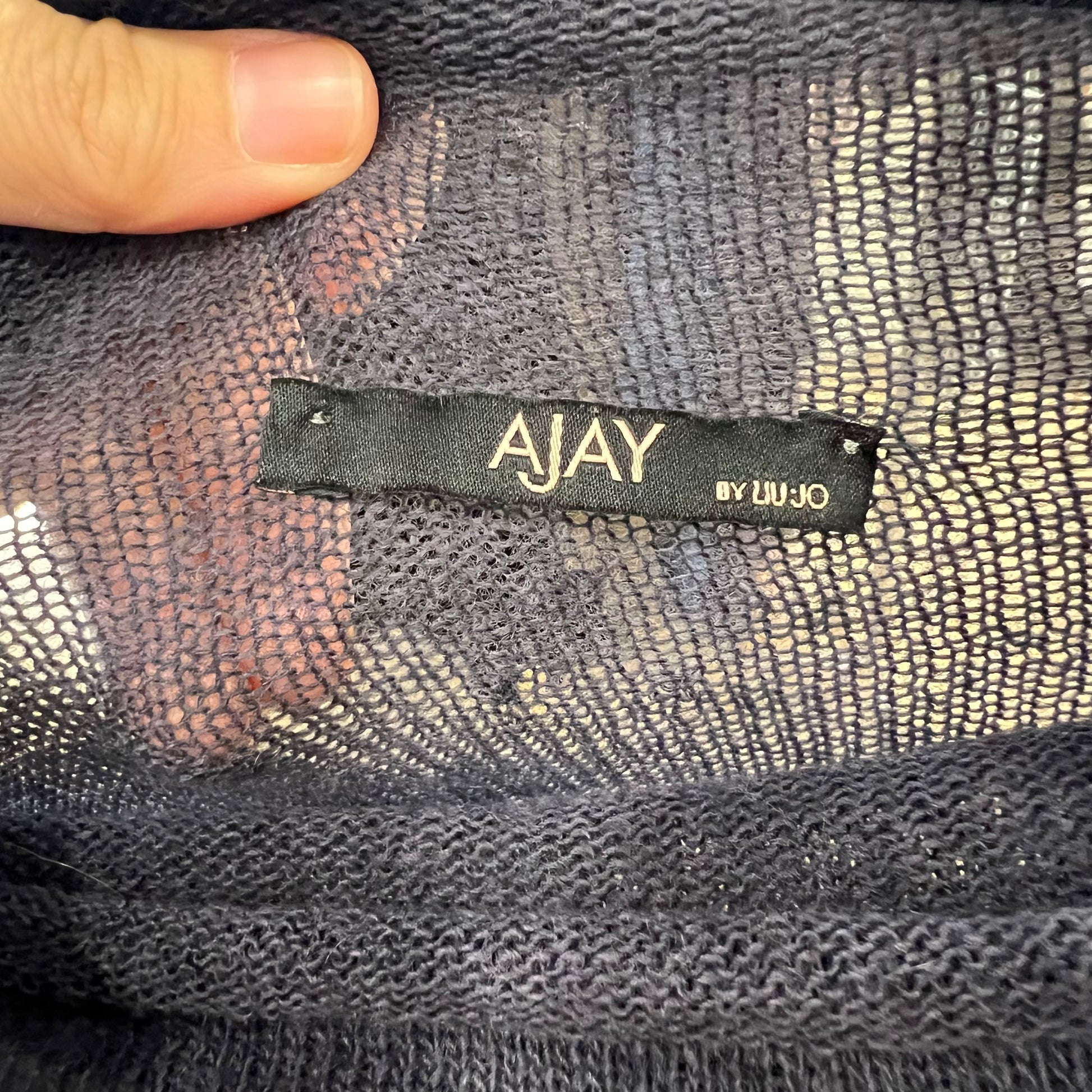 Close-up of a 'AJAY by Liu Ju' label on textured fabric