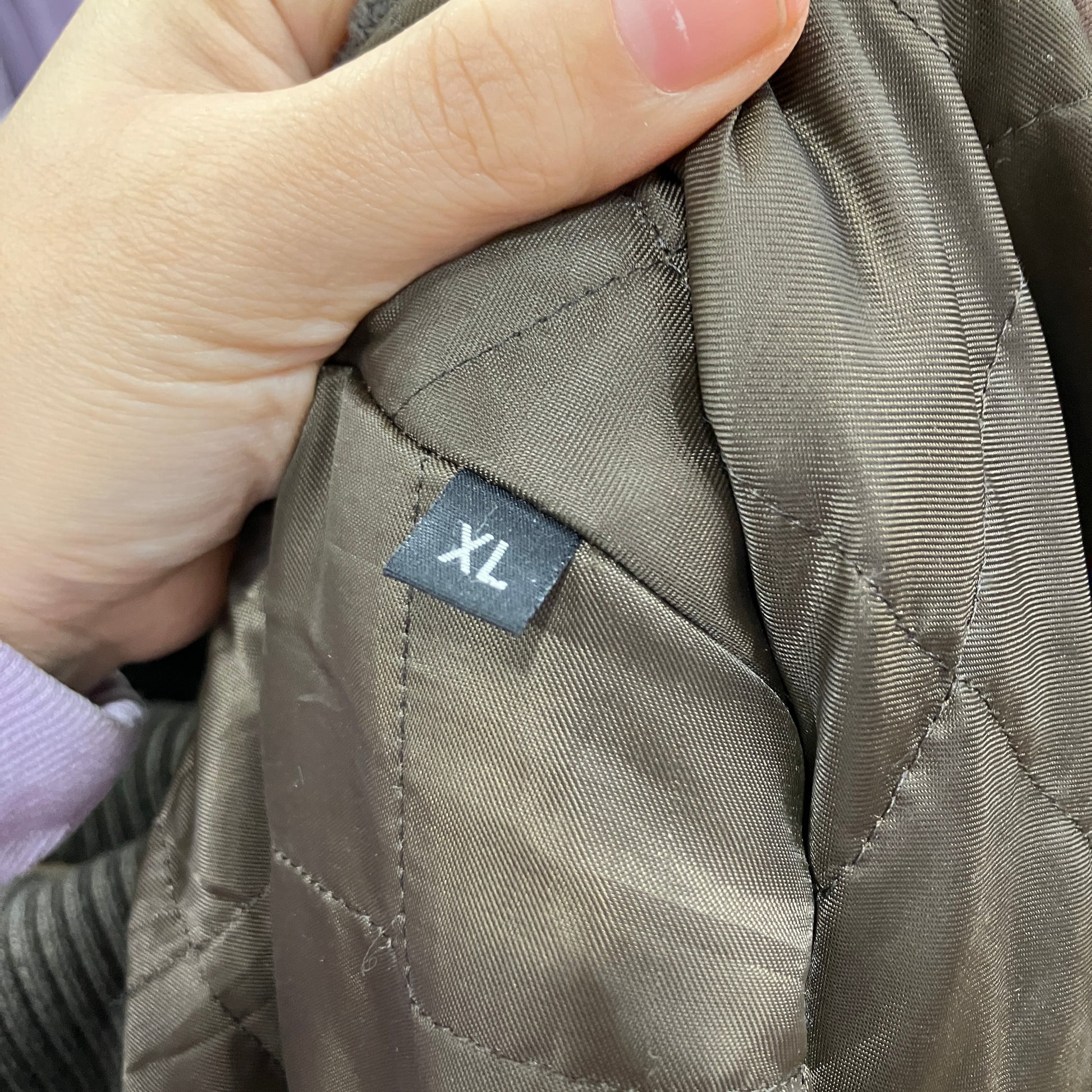 Hand holding a brown jacket with an XL size label