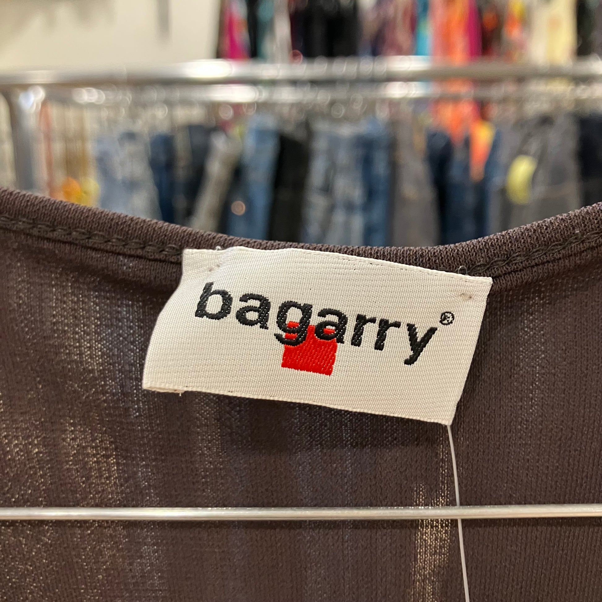 Close-up of a 'bagarry' label on a brown fabric with a clothing rack in the background
