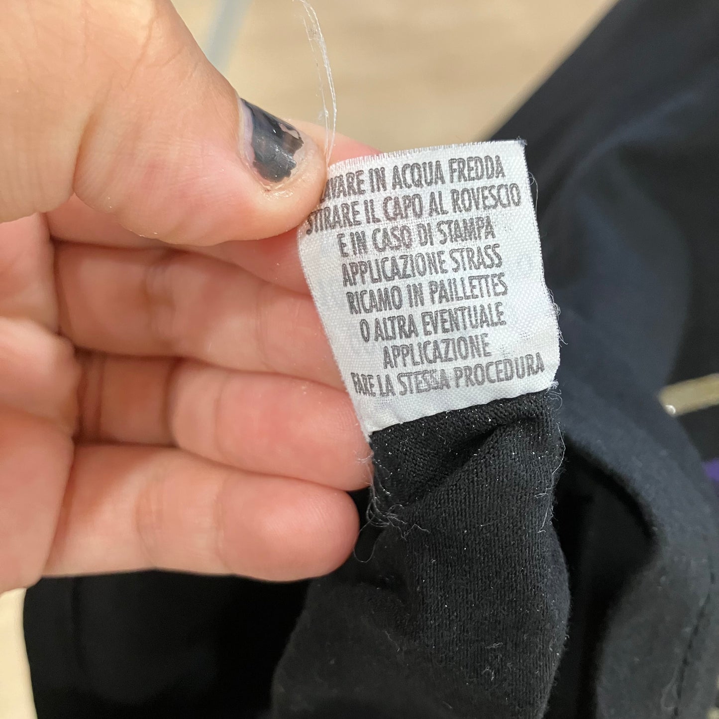 Hand holding a clothing label with text on a black garment