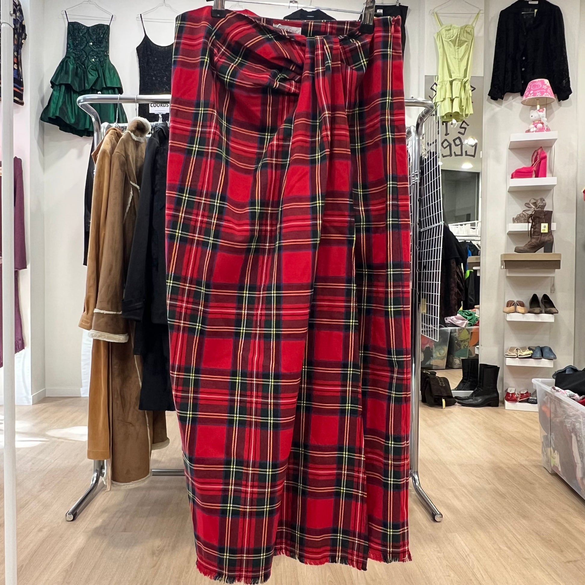 Red plaid skirt on a clothing rack in a store setting with various garments and shoes in the background