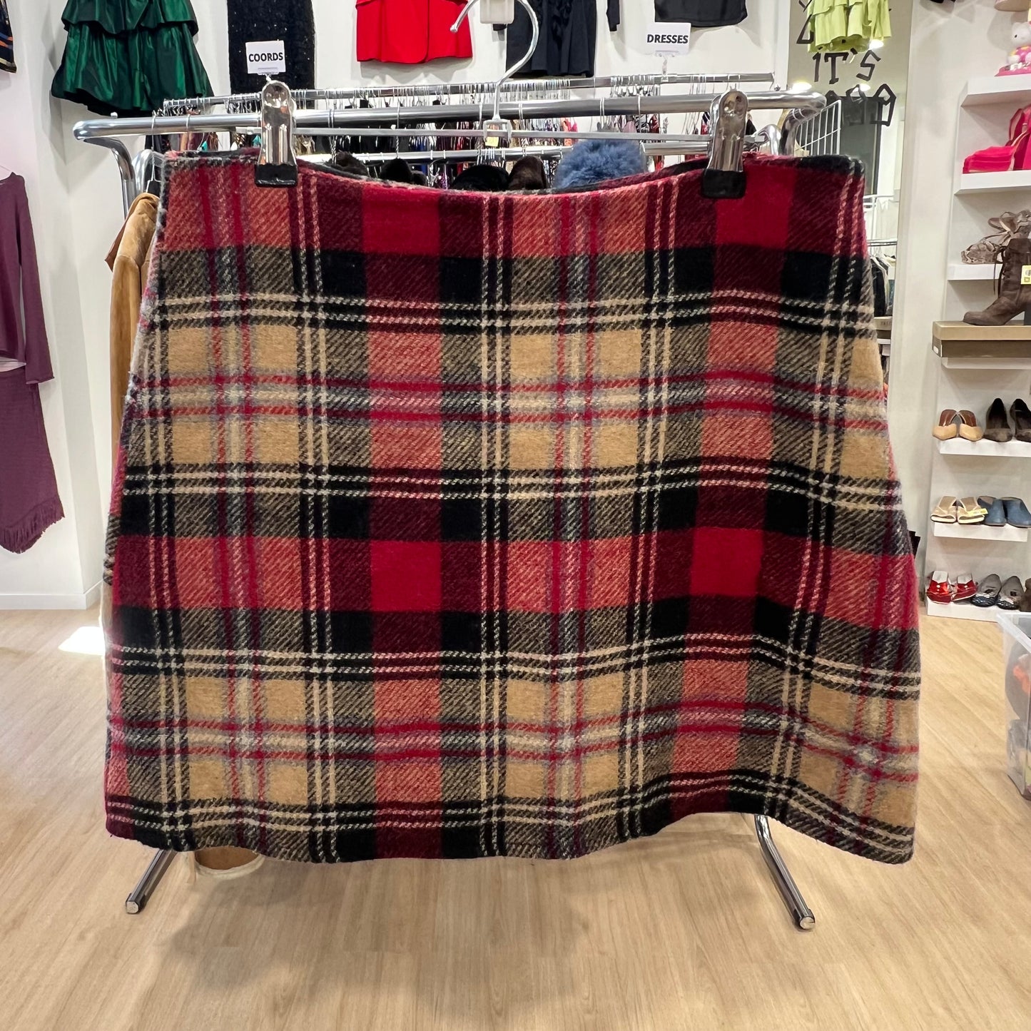 Plaid skirt on a rack in a store setting with clothing and shoes in the background