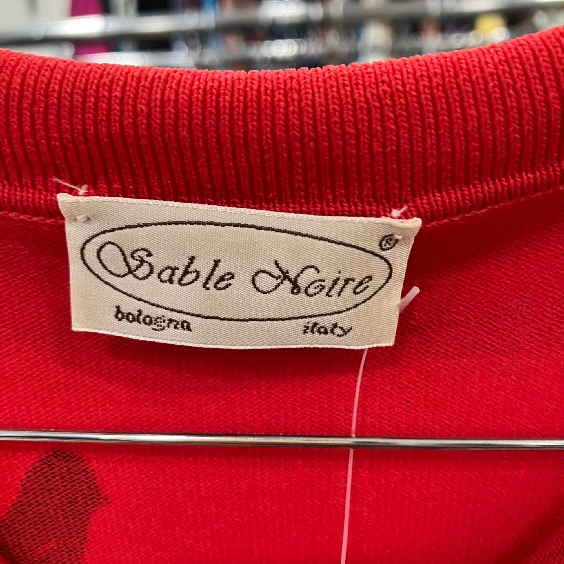 Close-up of a red garment with a 'Sable Noire' label on a blurred background