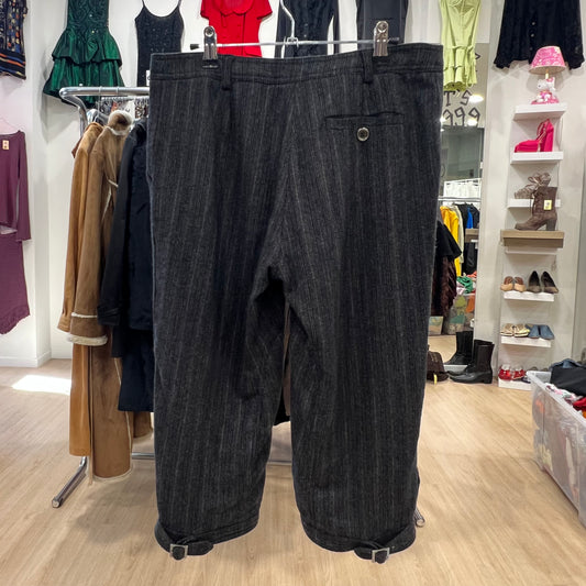 Black pinstripe pants hanging on a rack in a store setting with clothing and shoes in the background