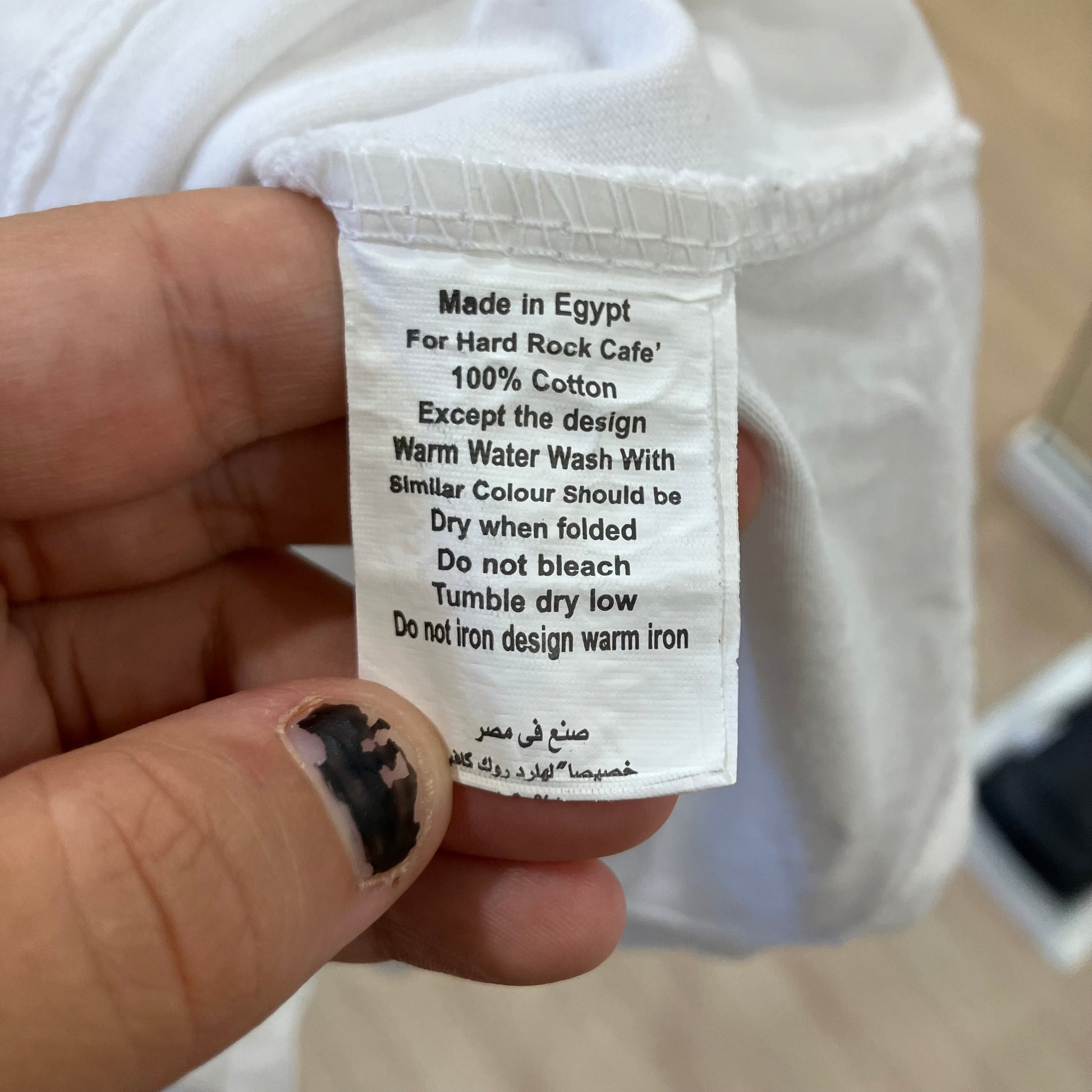 Clothing label held by a hand with text on it, against a blurred background