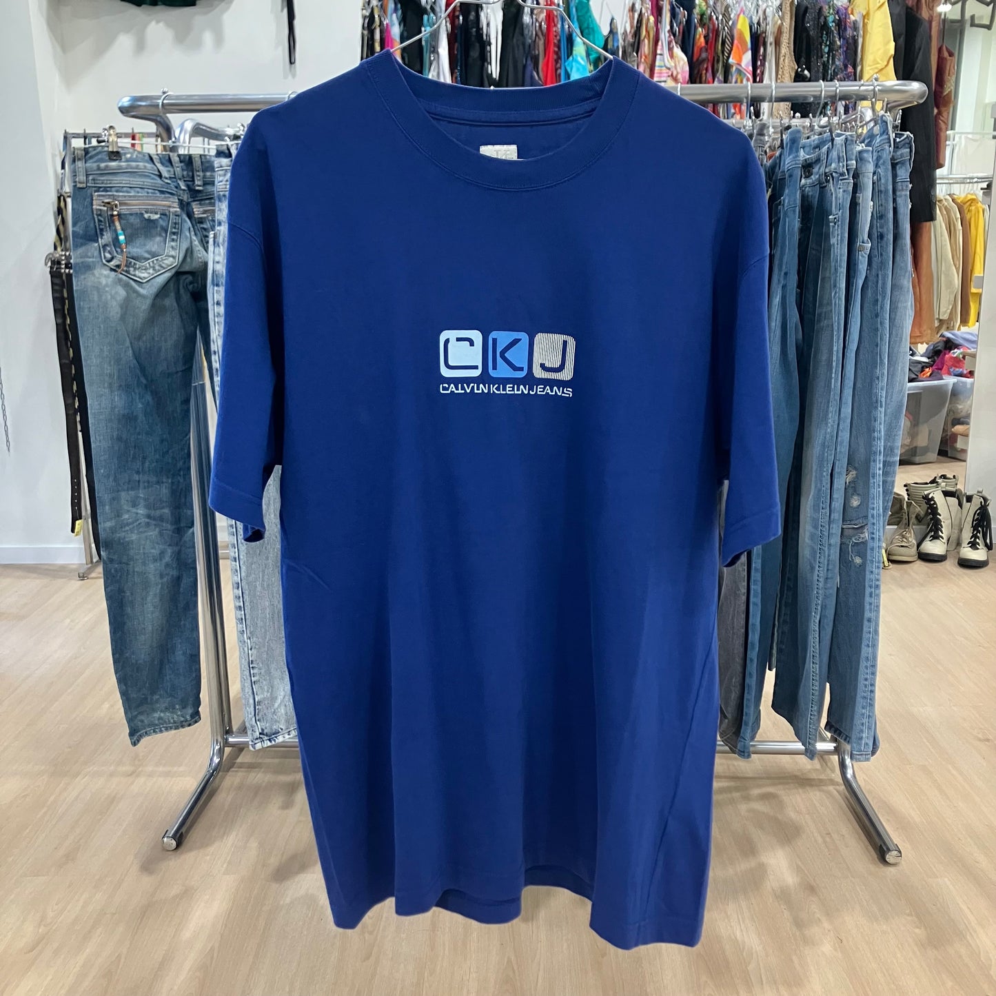 Blue t-shirt with Calvin Klein Jeans logo on a clothing rack with jeans in the background