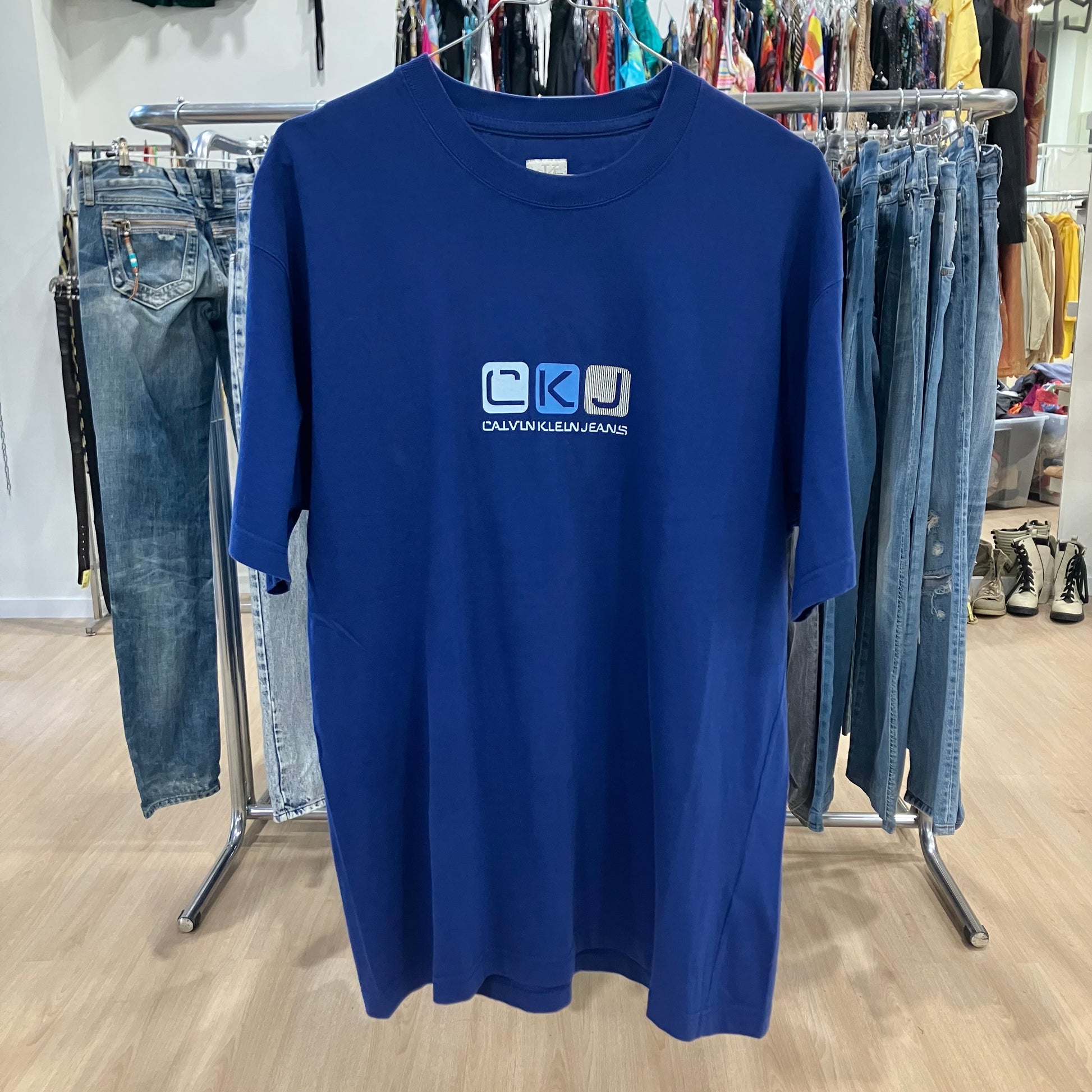 Blue t-shirt with Calvin Klein Jeans logo on a clothing rack with jeans in the background