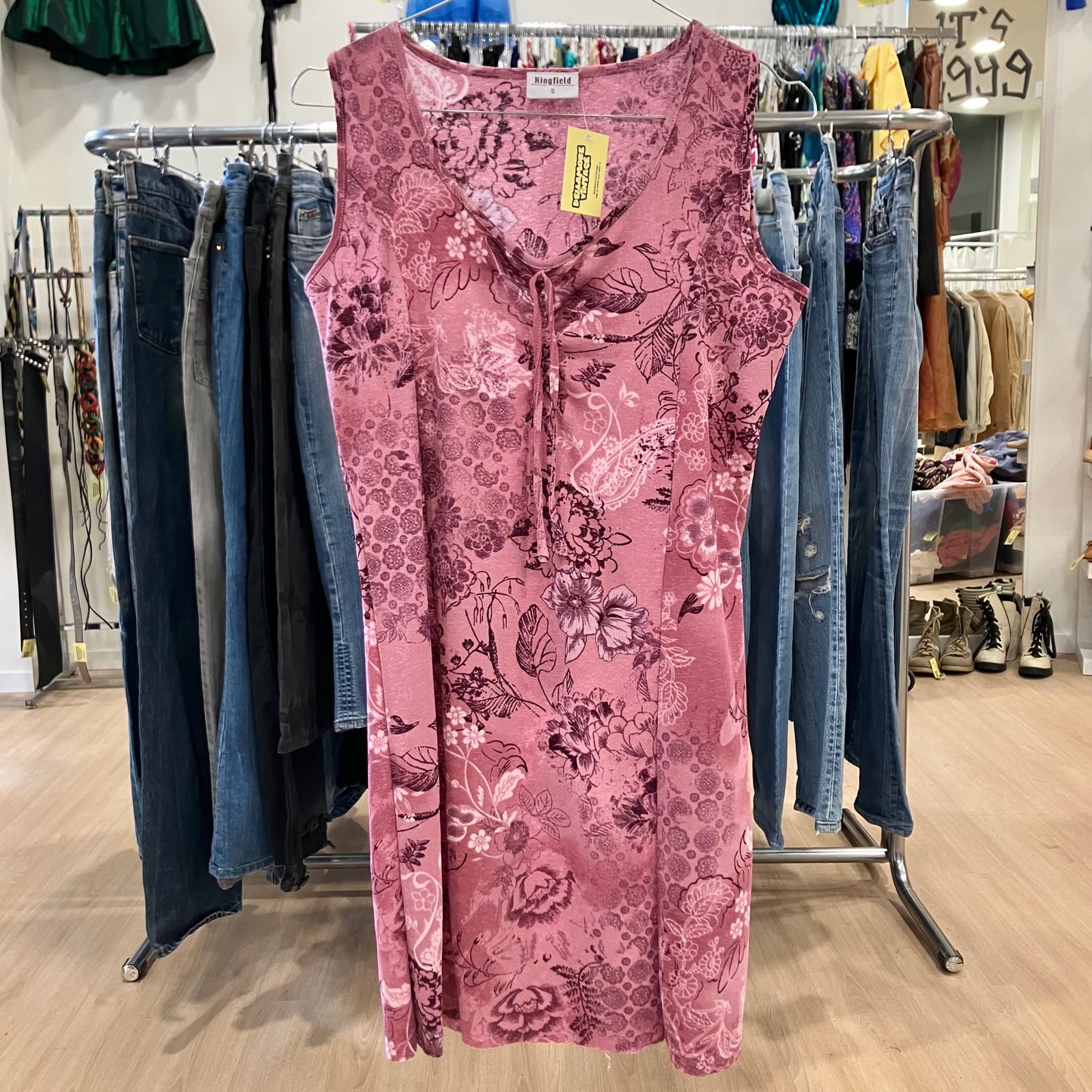 Pink floral dress on a rack with jeans in a store setting