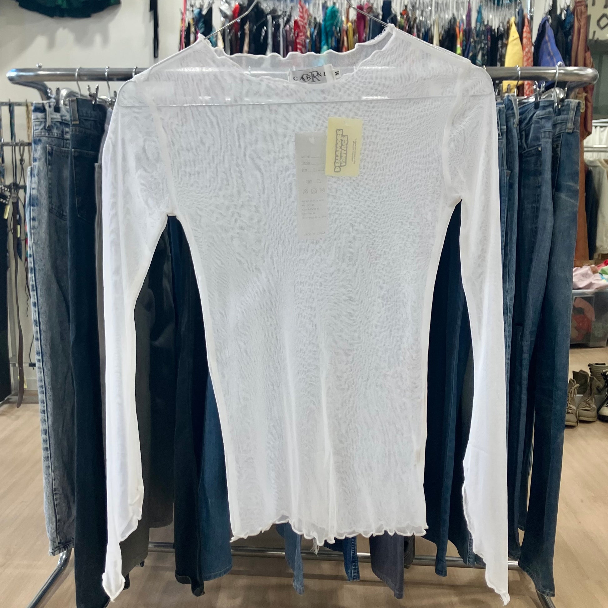 White long-sleeve shirt on a rack with jeans in a store setting