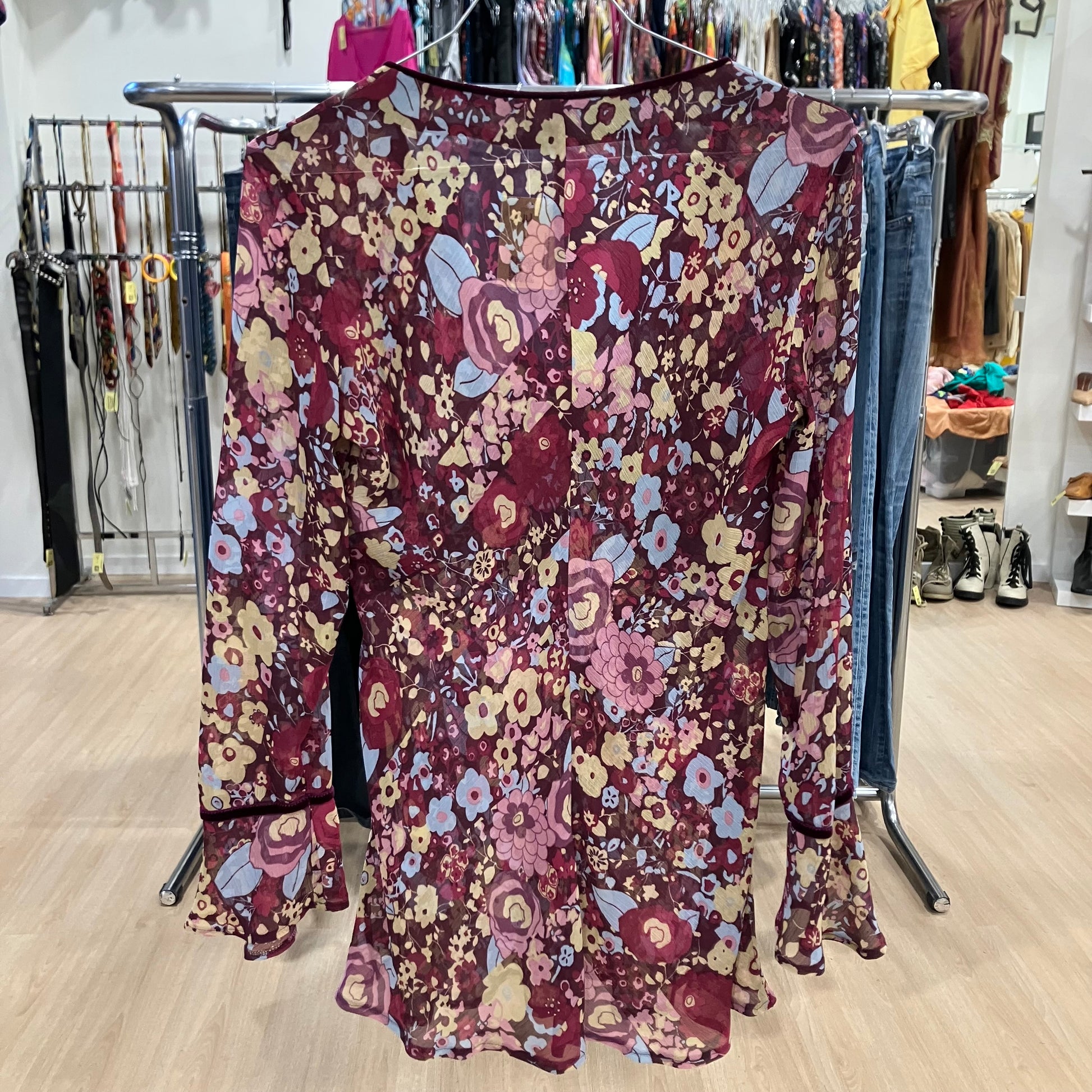 Sheer floral long-sleeve blouse with a V-neck hanging on a rack inside a clothing store
