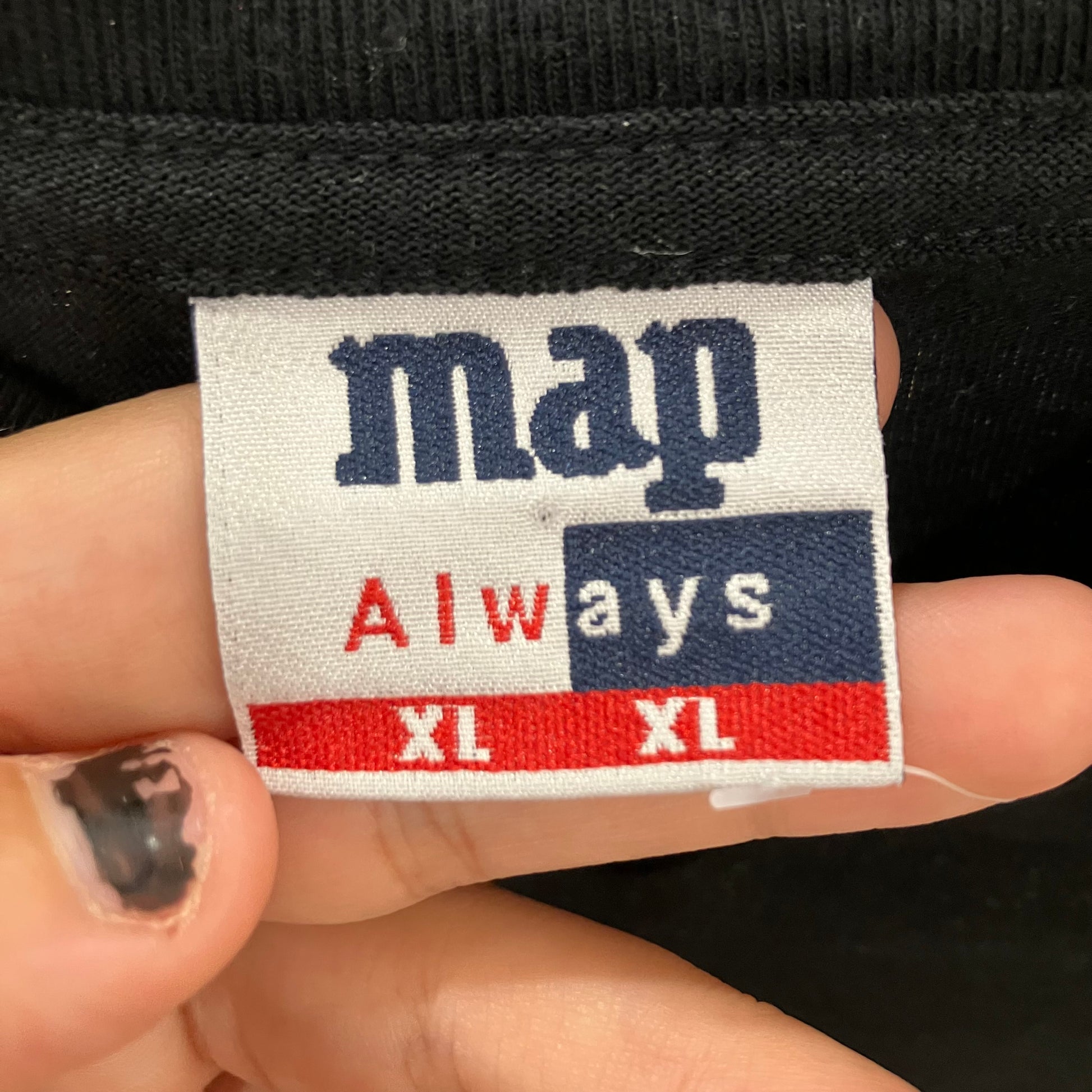 Fabric tag with 'map Always XL XL' text held between fingers against a black background