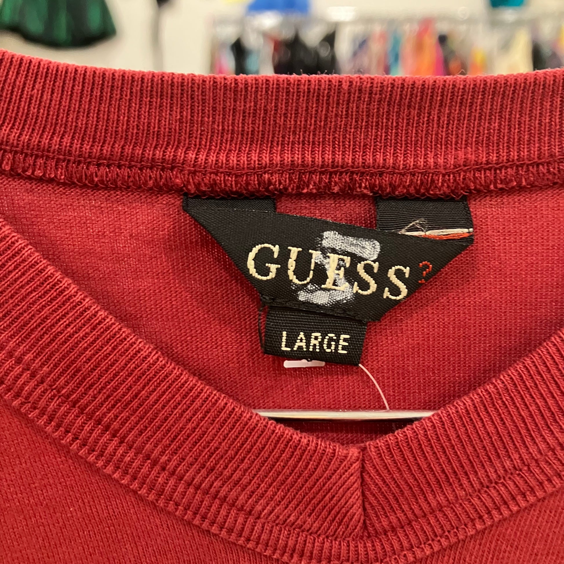 Close-up of a Guess label on a red garment with a blurred store background