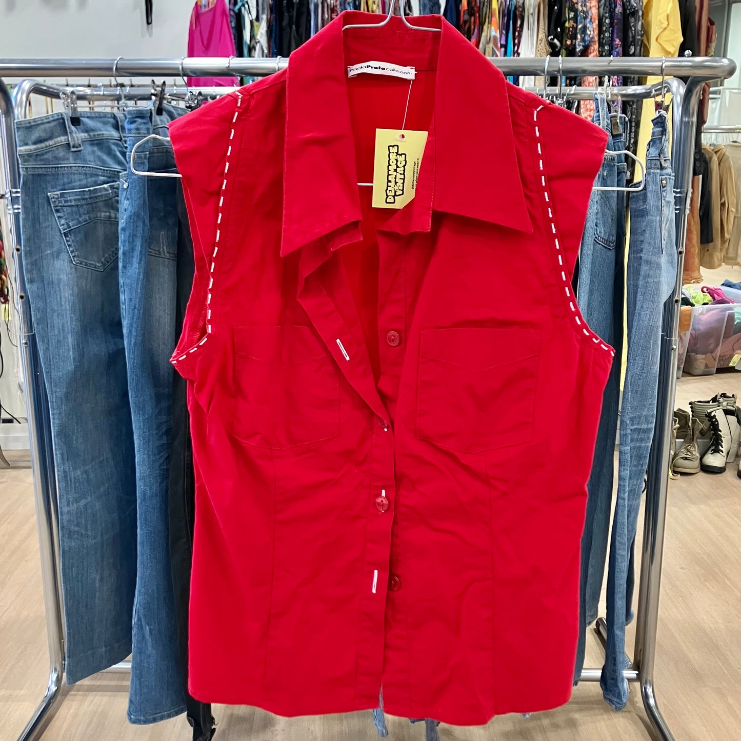 Red vest with a tag on a clothing rack with jeans in a store setting
