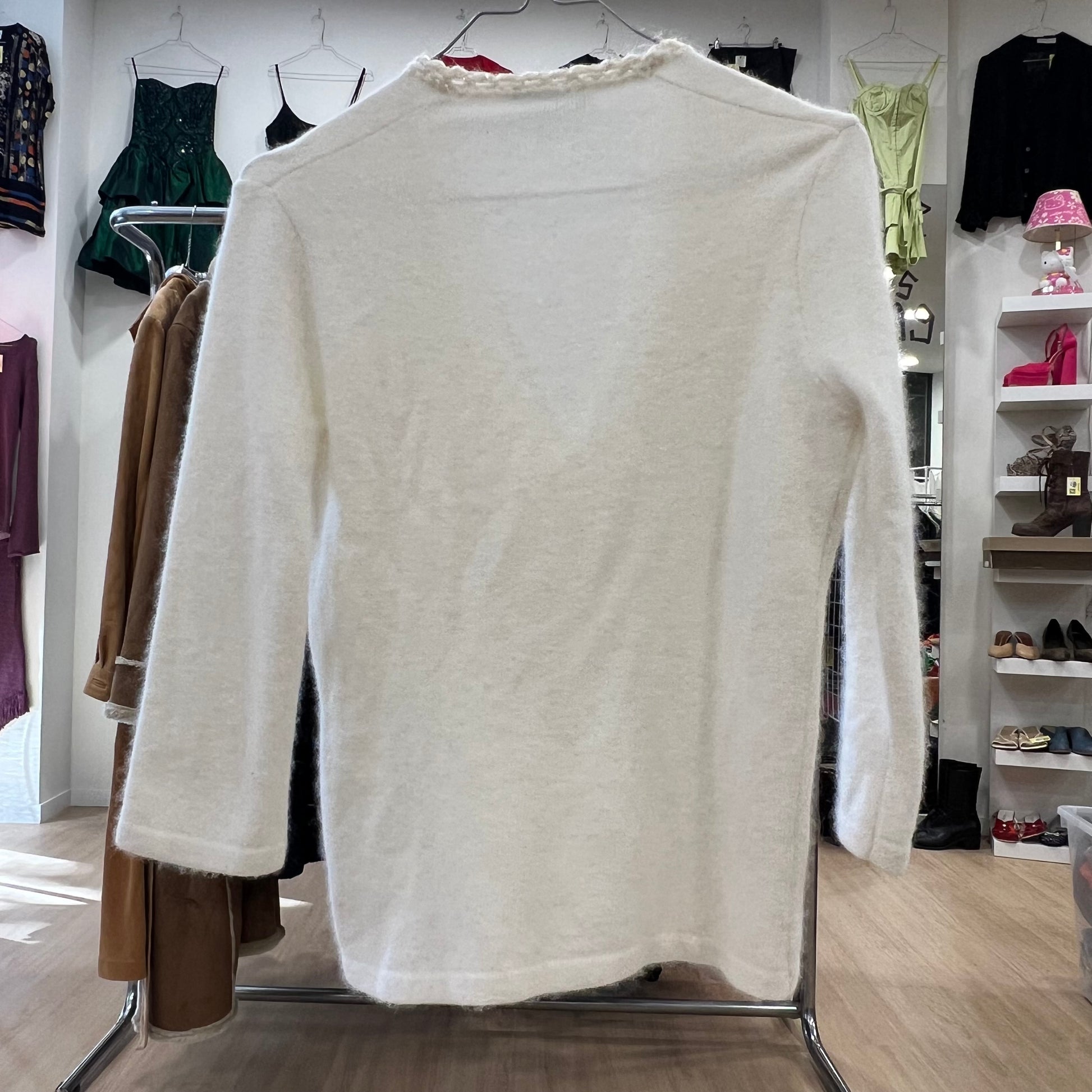 White sweater on a rack in a clothing store with various garments in the background