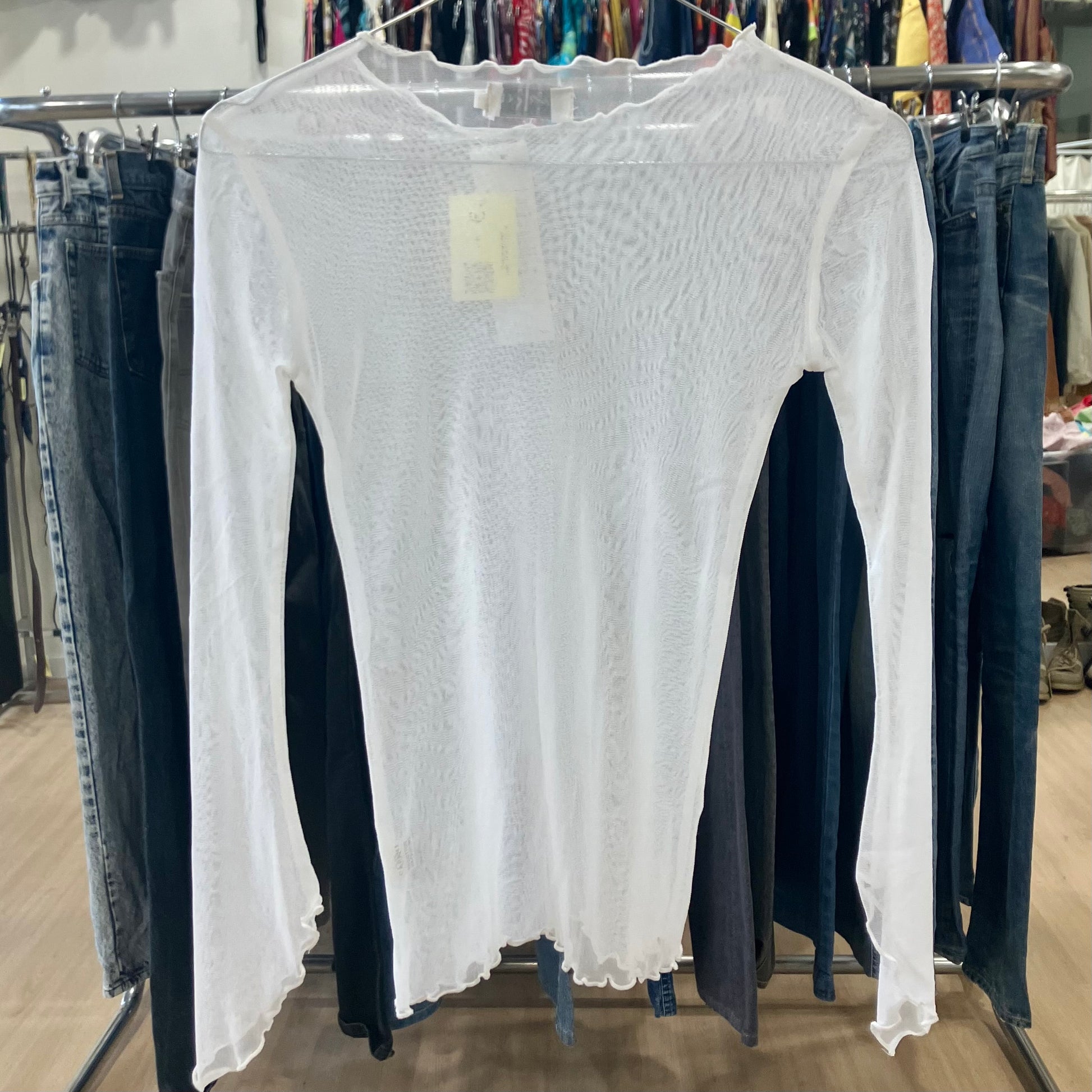 White long-sleeve top on a rack with jeans in a store setting