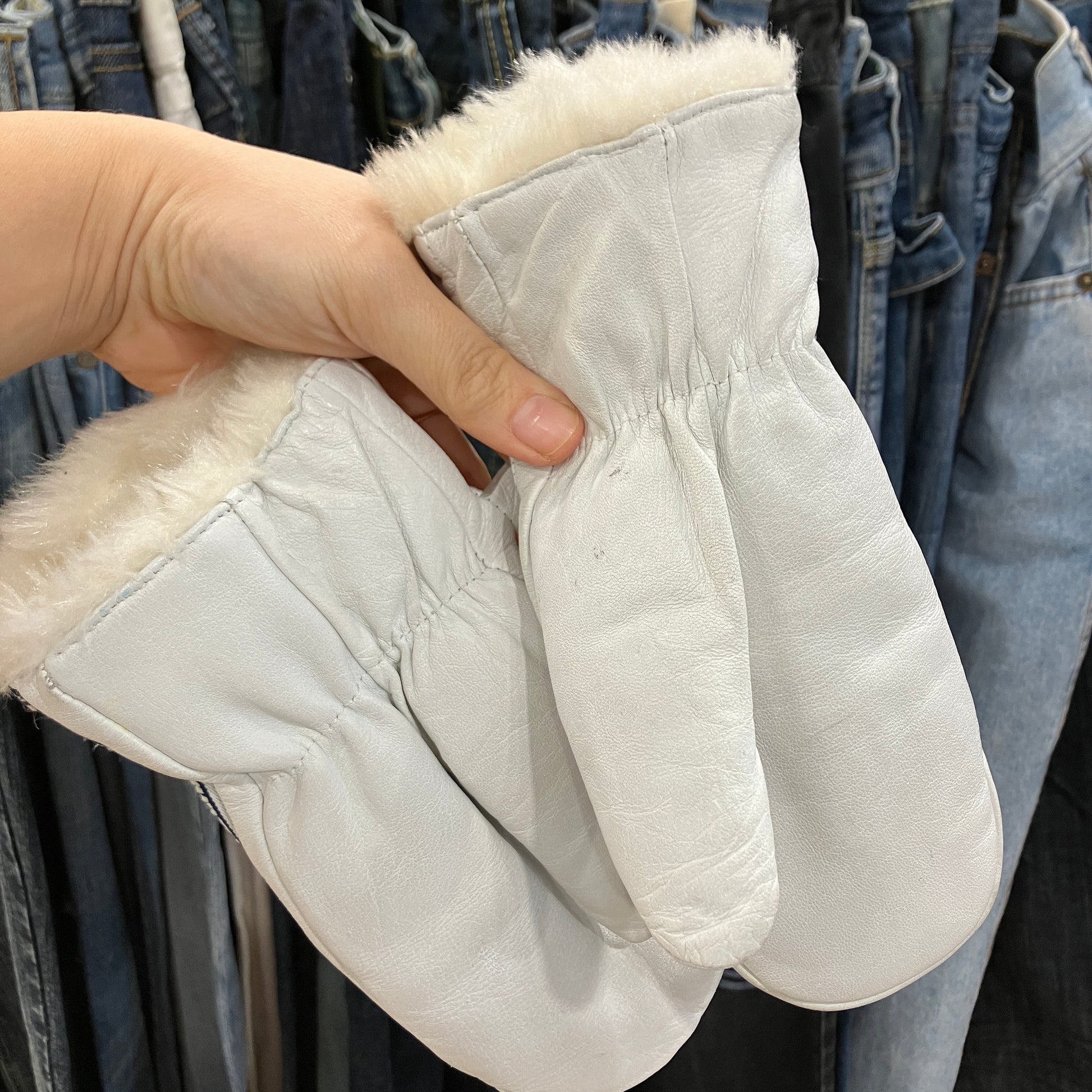 White mittens with fur lining held by a hand against a background of jeans