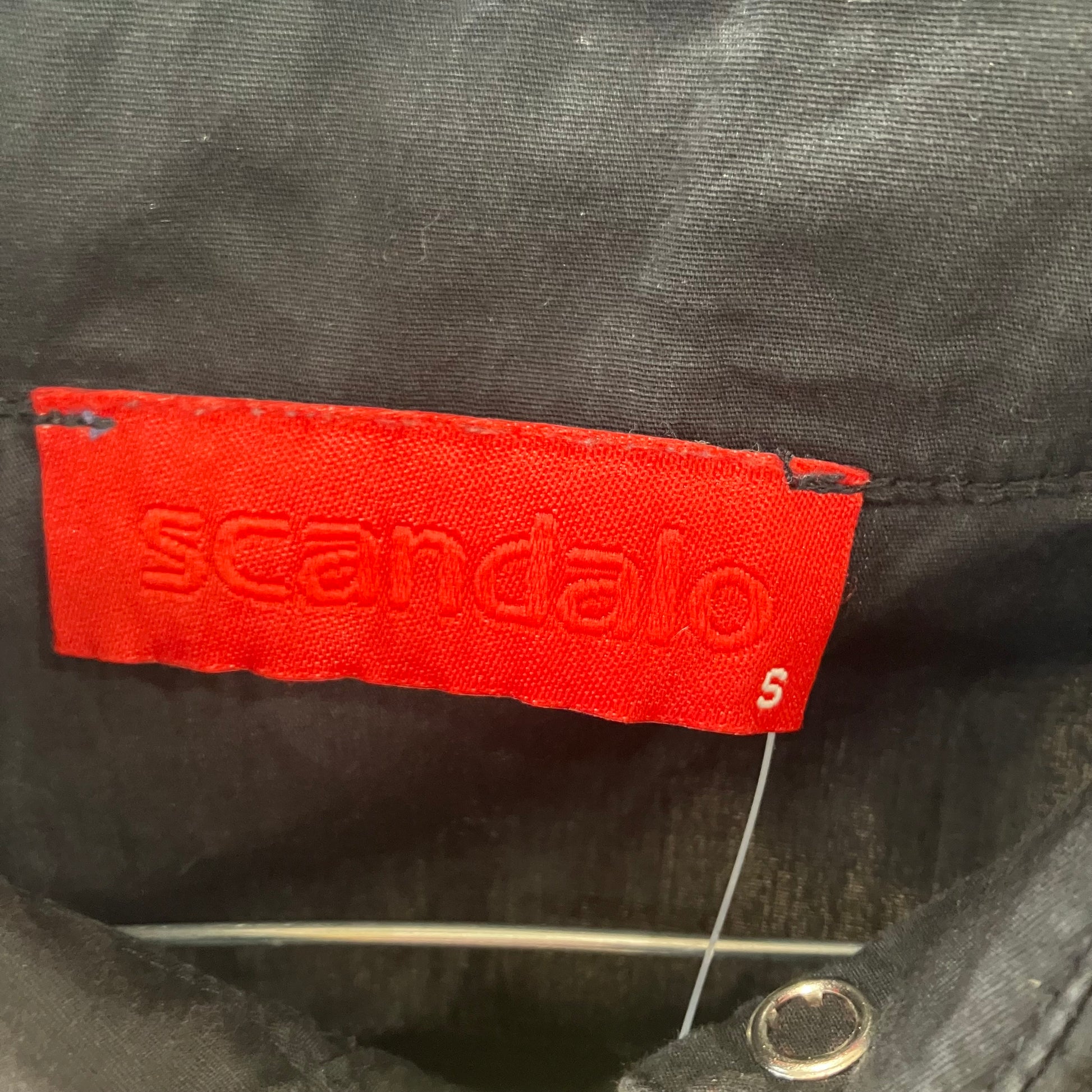 Red 'scandalo' label on a black shirt with a metal pin