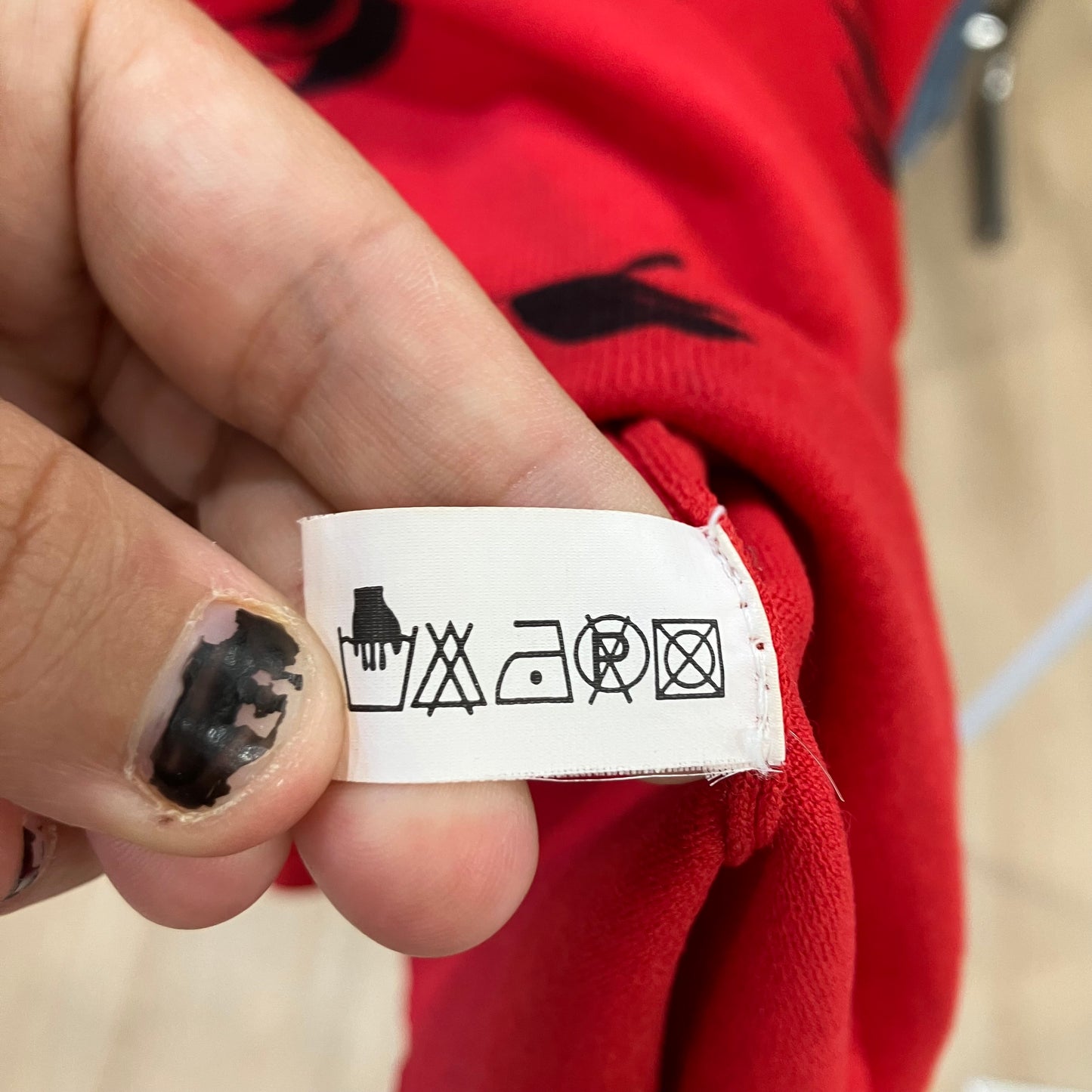 Hand holding a clothing label with care instructions against a red garment background