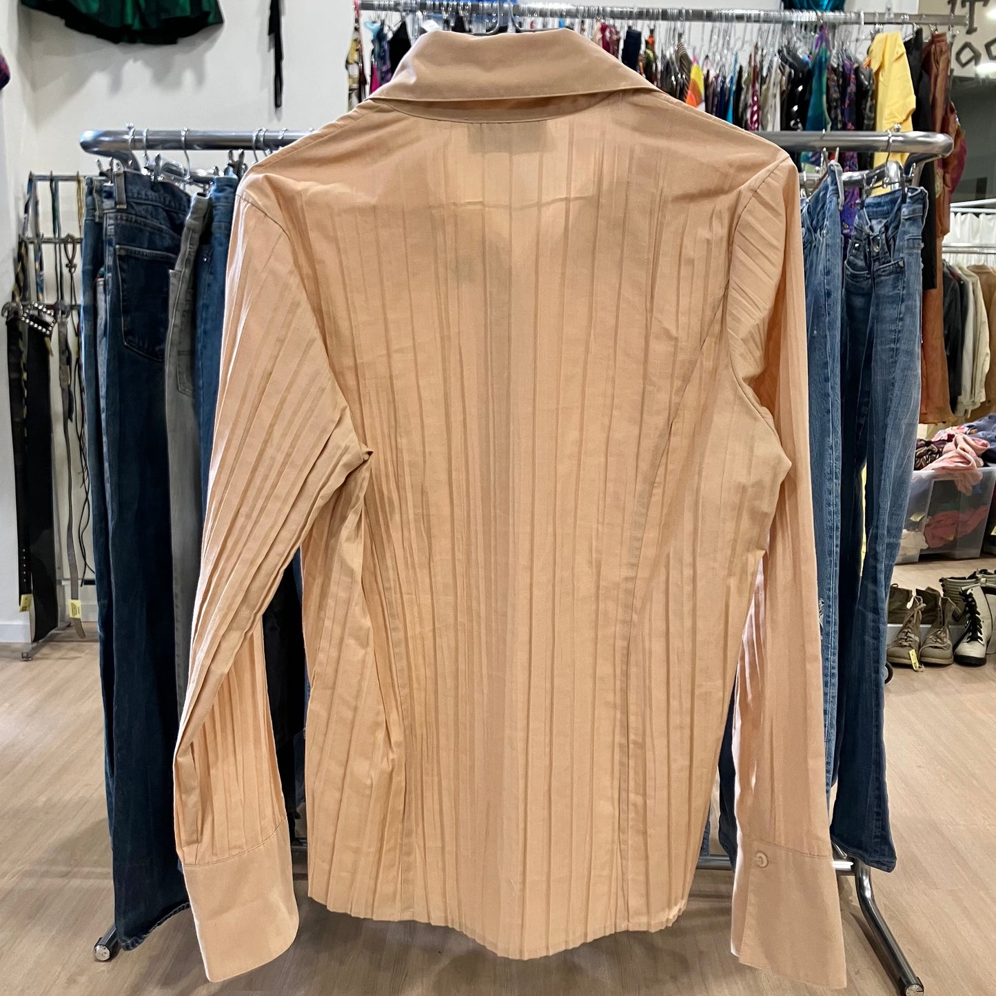 Beige shirt on a hanger with clothing racks and jeans in the background