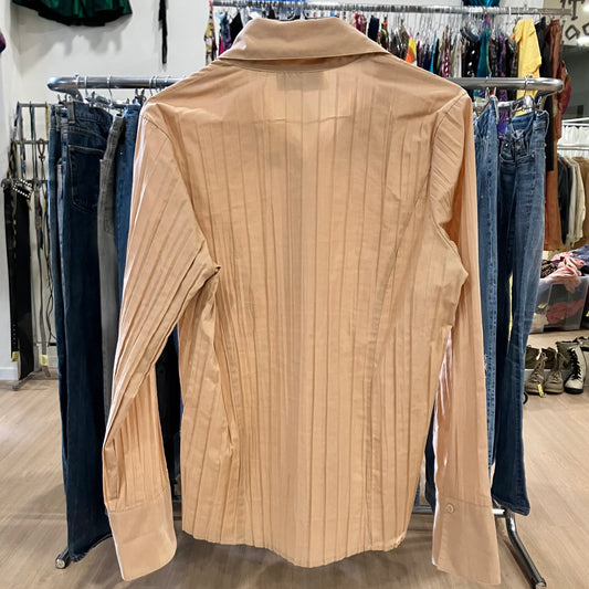 Beige shirt on a hanger with clothing racks and jeans in the background