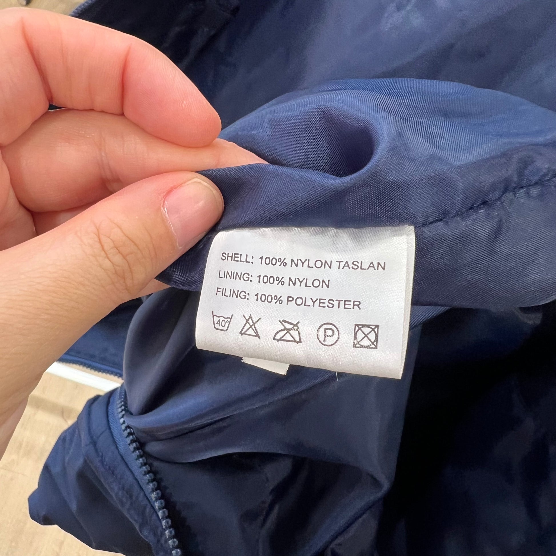 Hand holding a clothing label on a blue jacket with text and symbols