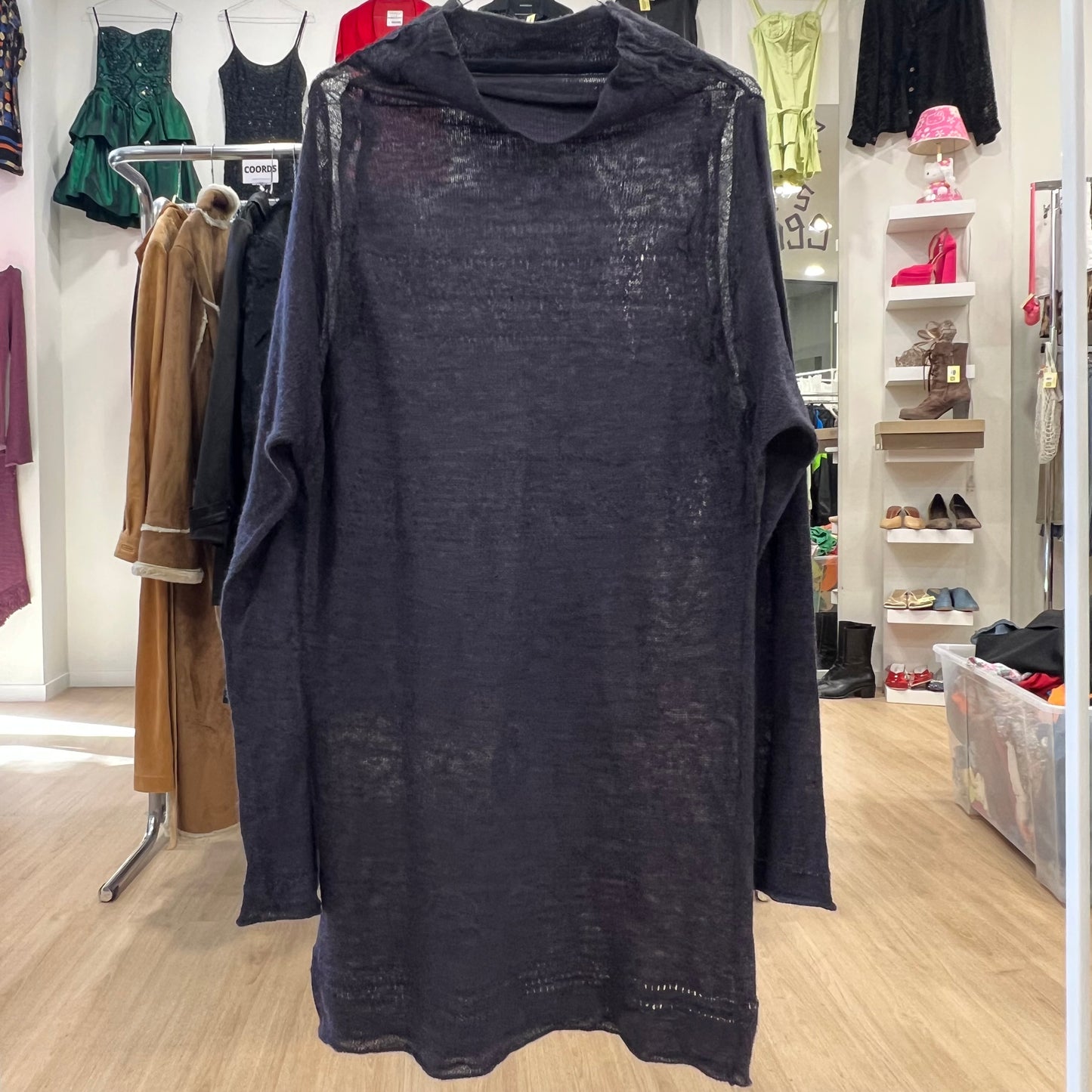 Dark dress on a hanger in a store setting with clothing racks and shelves in the background