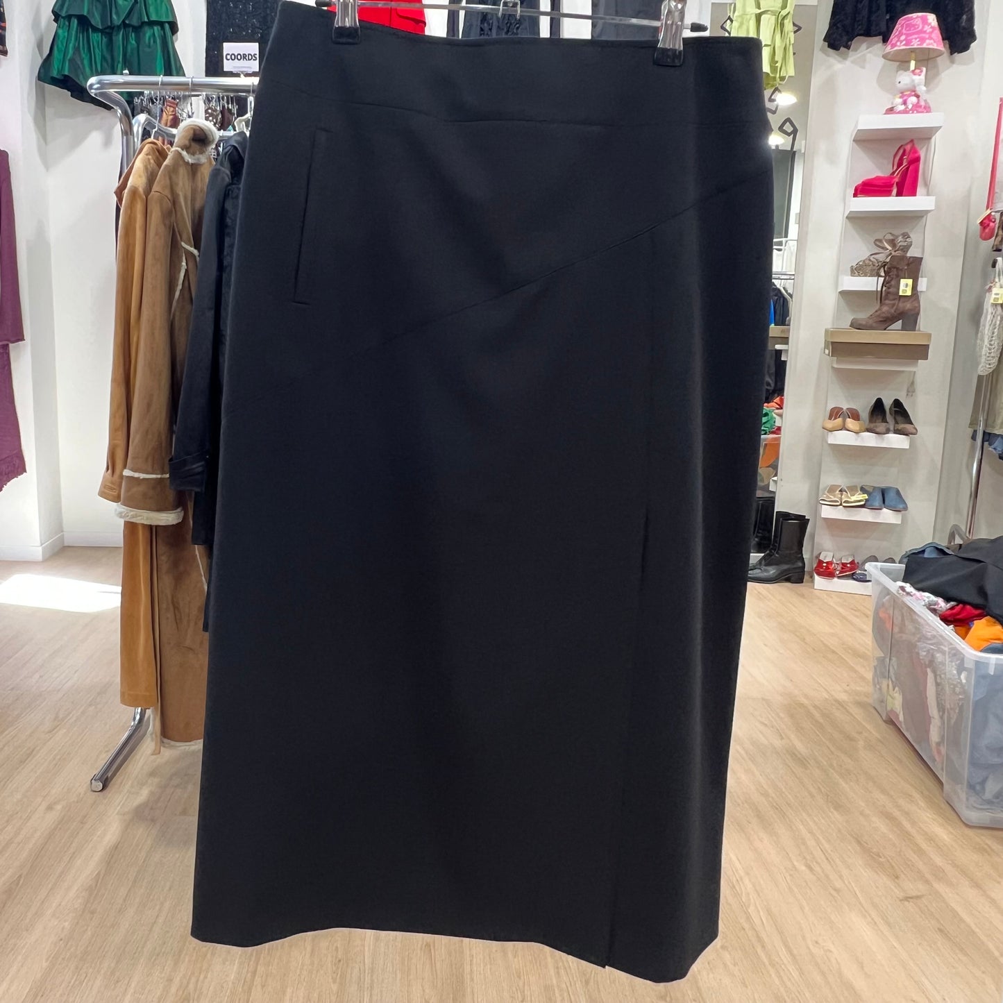 Black skirt on a hanger in a store setting with clothing racks and shelves in the background